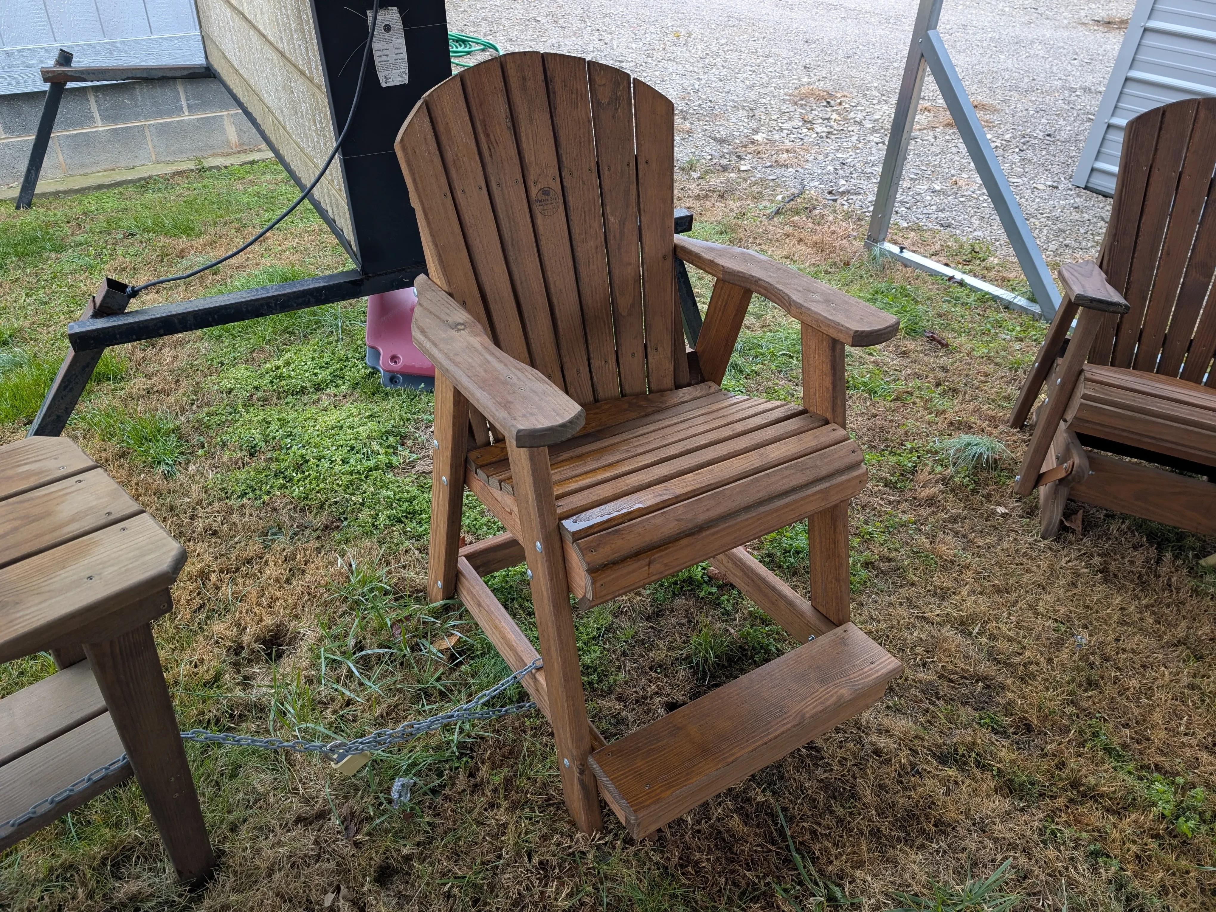 a wood chair with a foot rest attached. It is in the grass and there is furniture around it