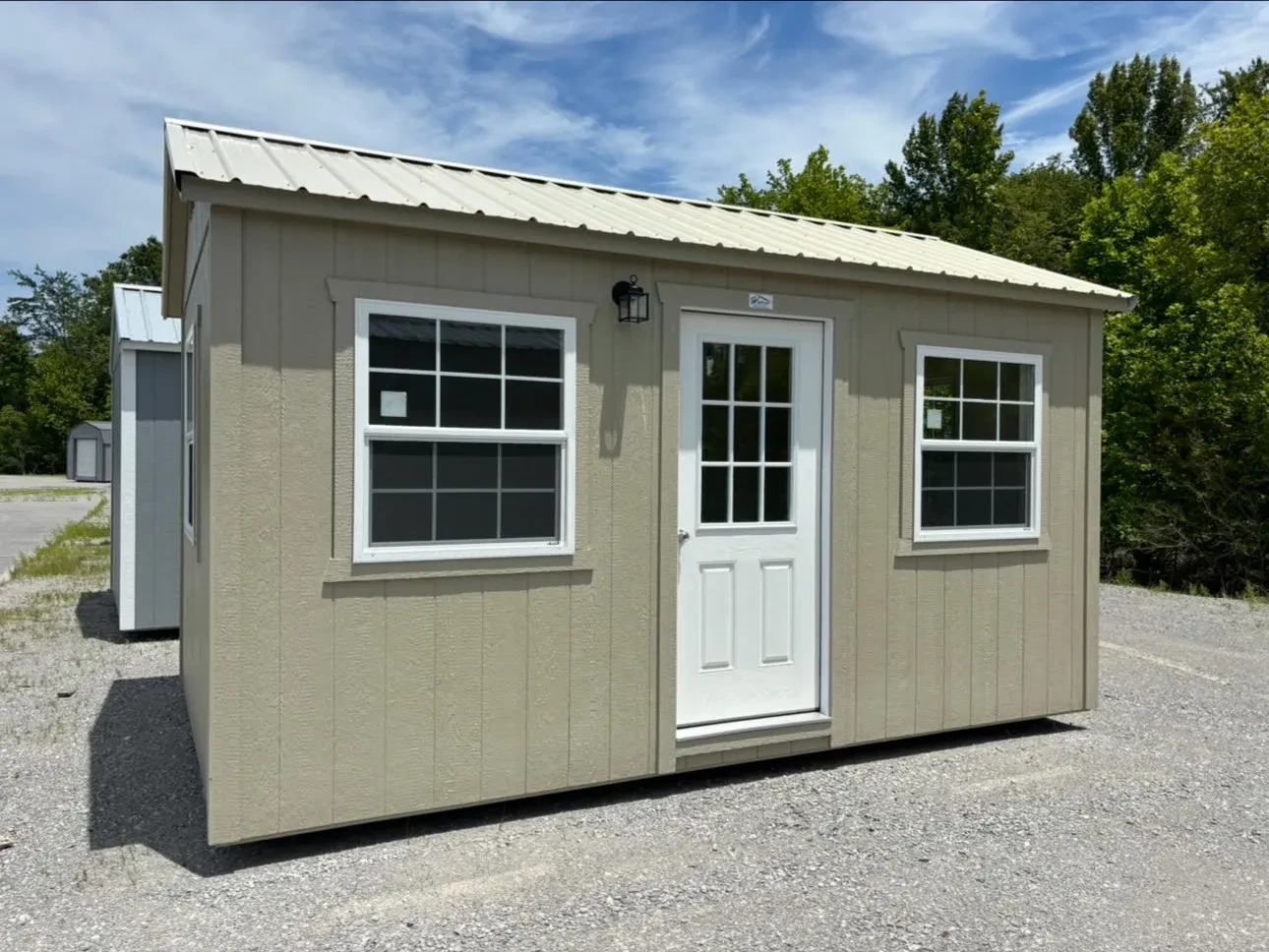 A stone colored shed with a walk-in door, two vinyl insulated glass windows, and an exterior lamp