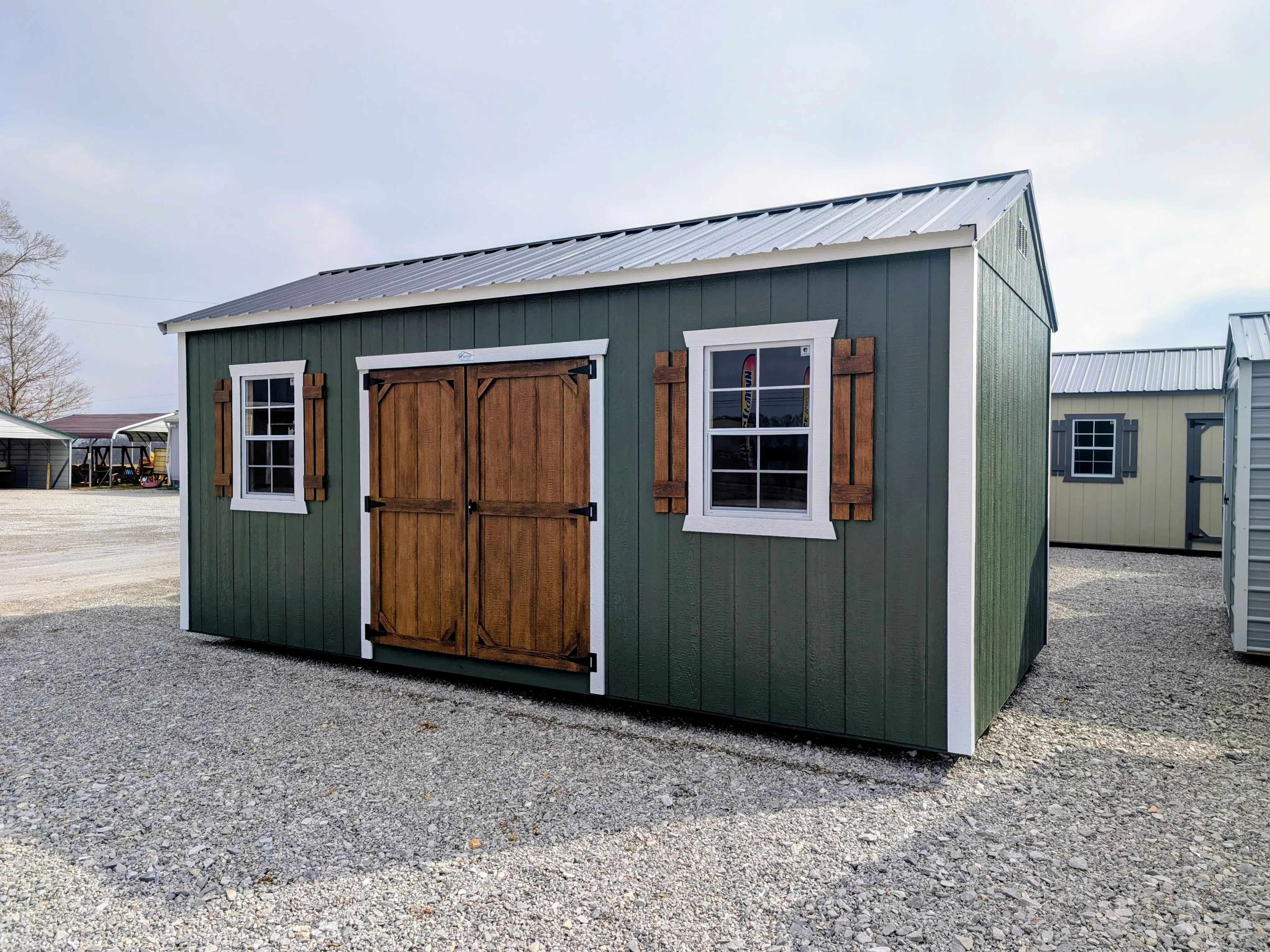 a green garden shed with two windows with shutters and double doors. The doors and shutters are wood stained