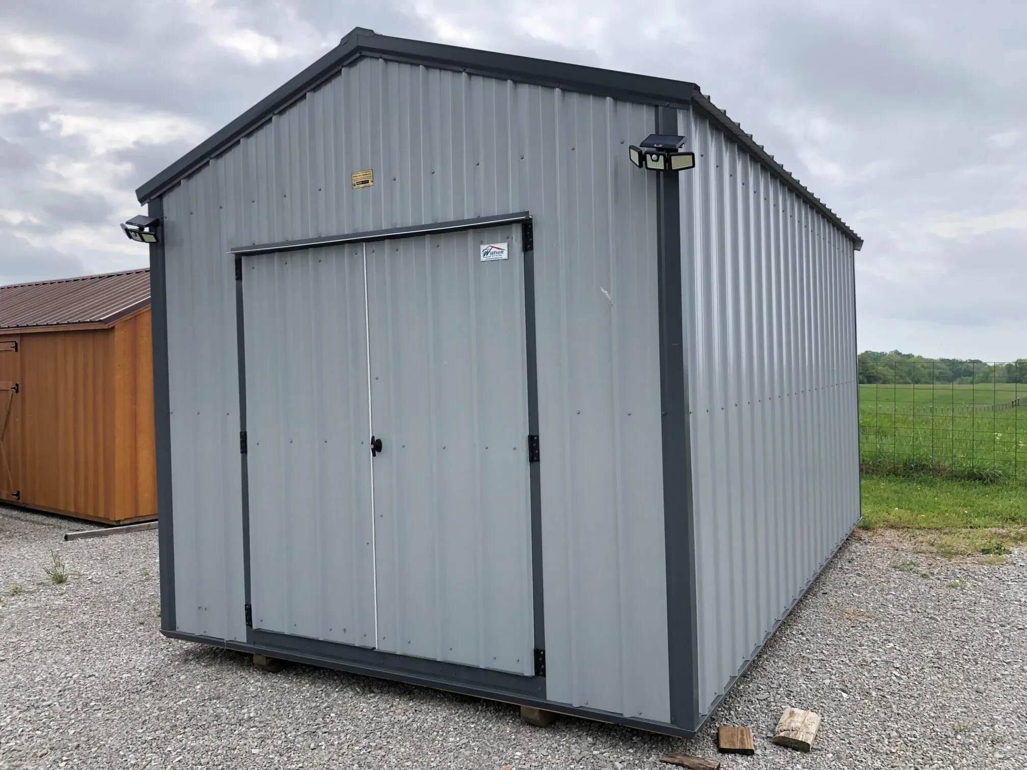the outside of a gray metal shed with double doors and lamps