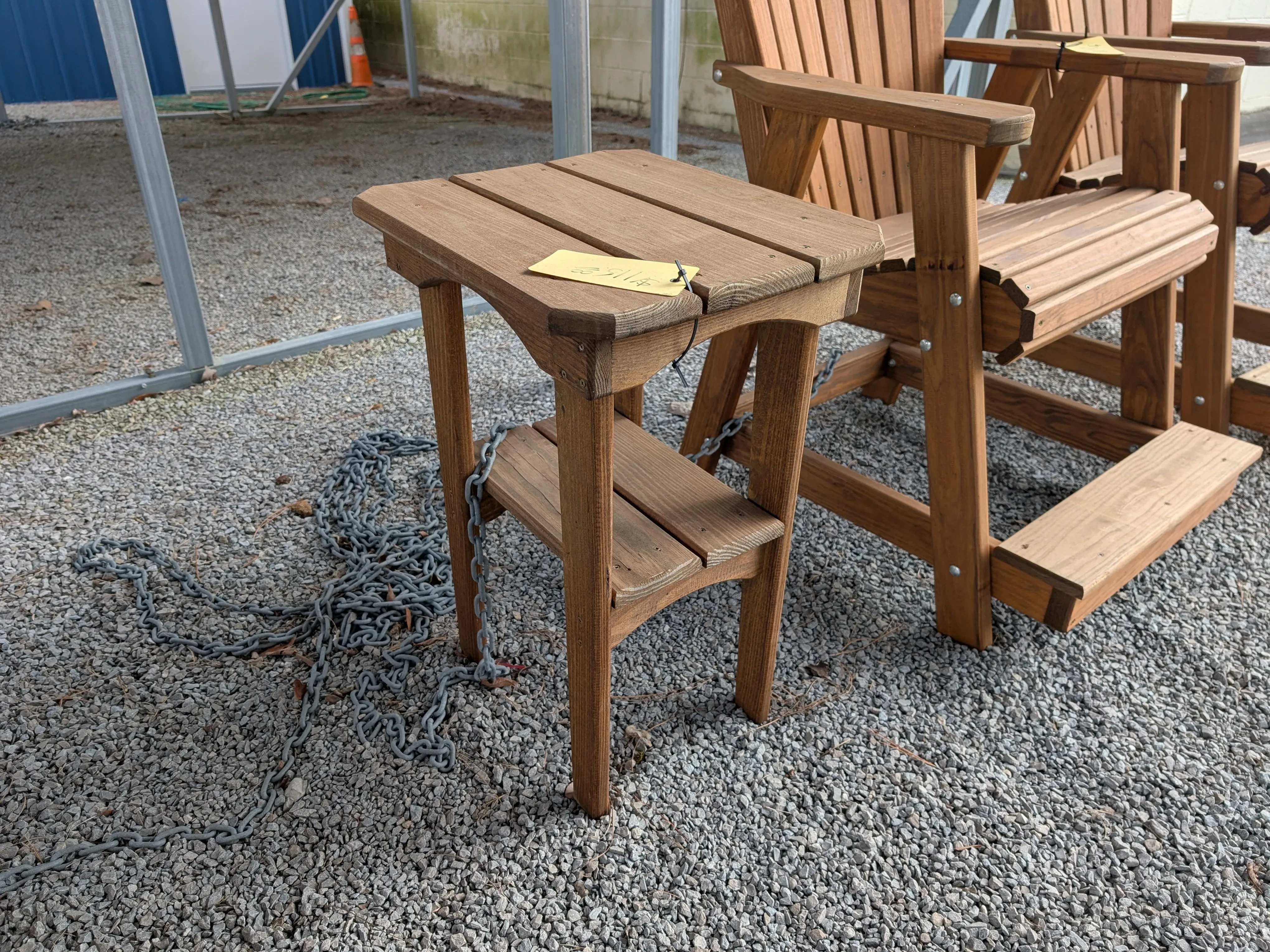 a small wood table. It is sitting in the gravel next o a chair