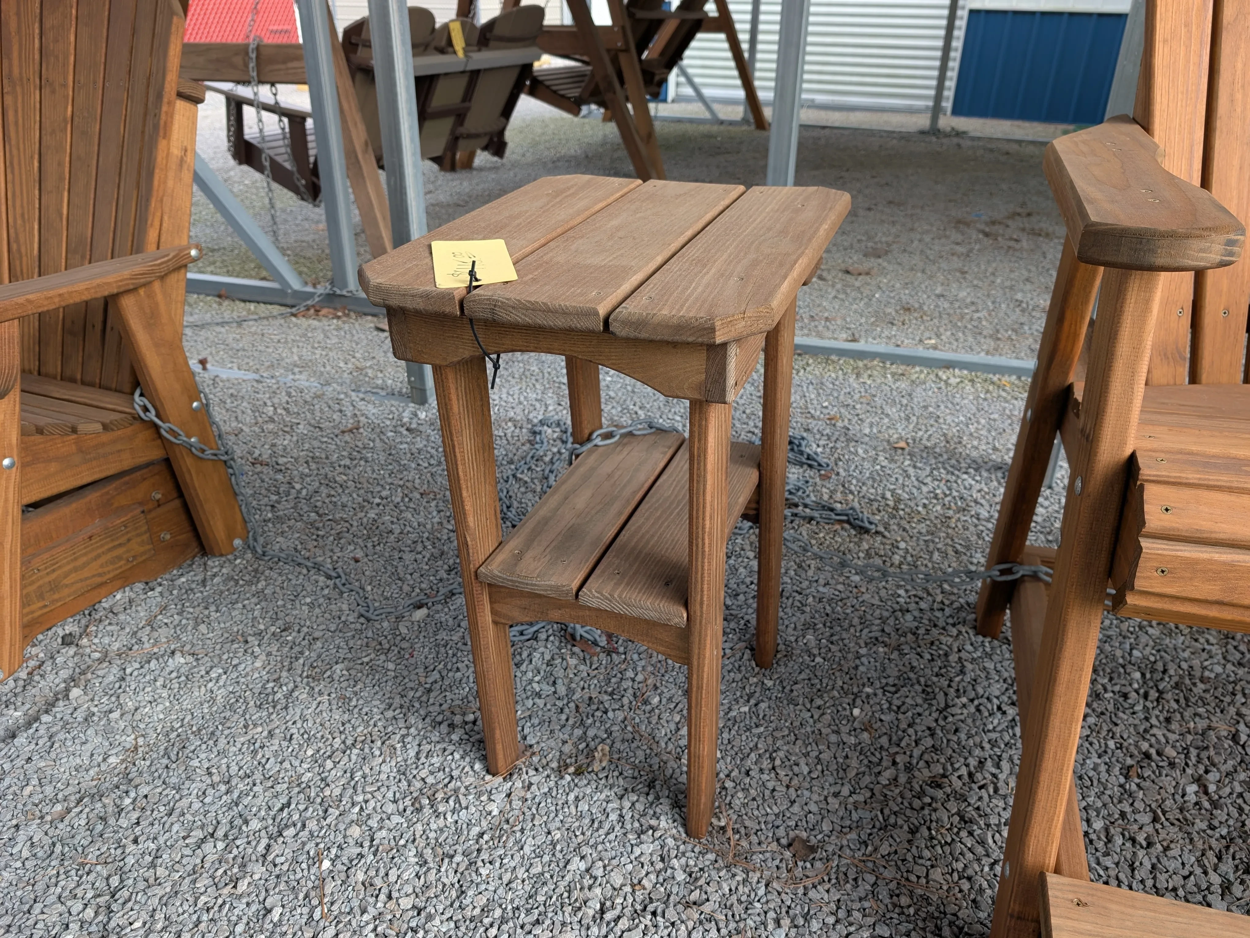 a small wood stained and sealed table sitting in the gravel. It has a yellow price tag on it.