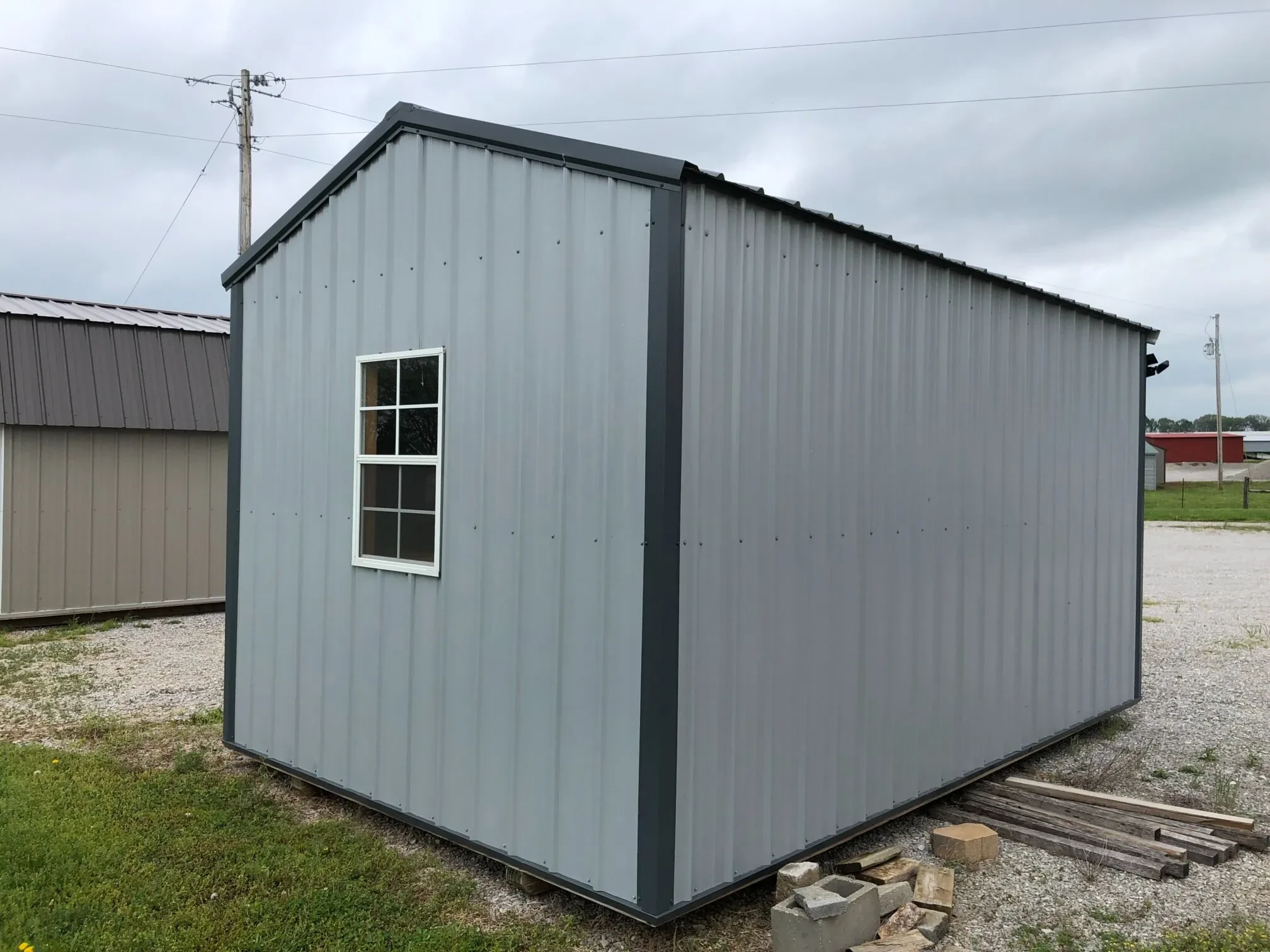 The rear view of a metal shed showing a window in the middle of the back wall.