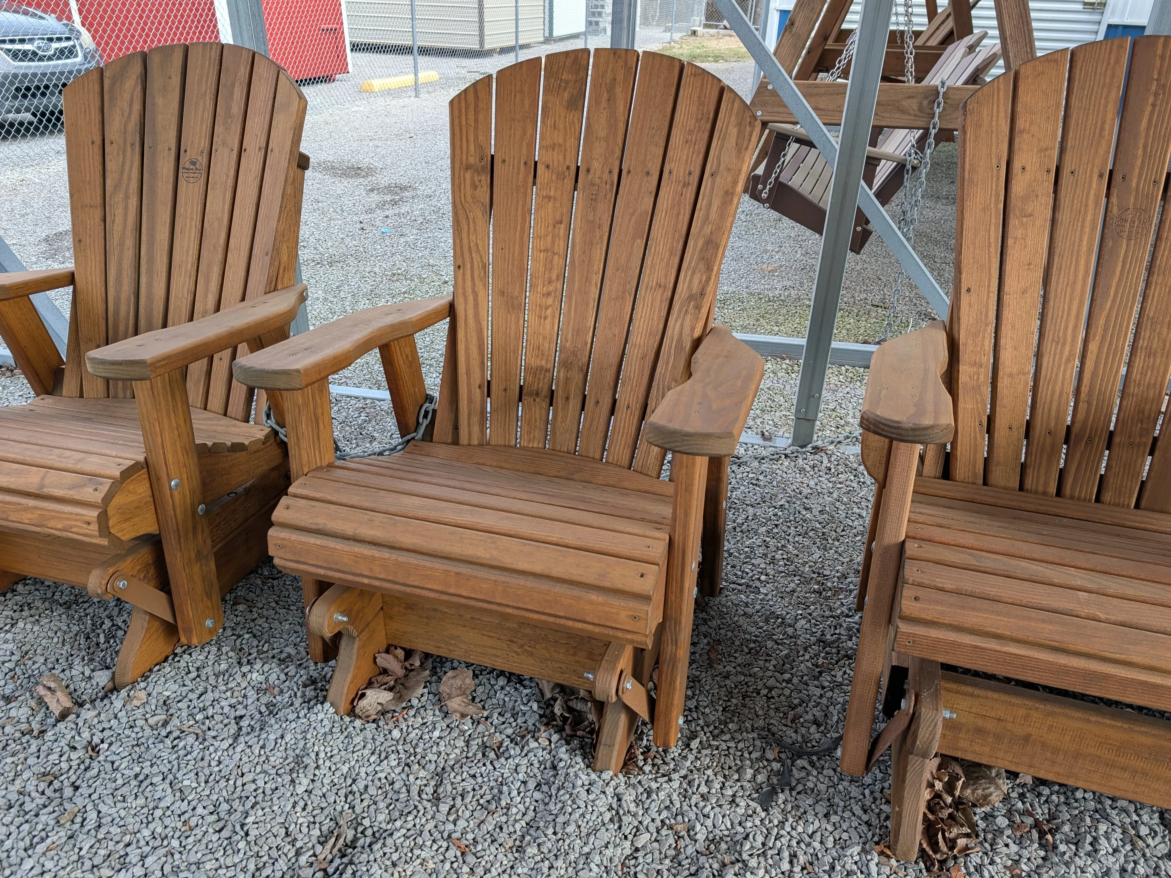 a wood chair sitting in the gravel. It has arm rests and is next to other furniture