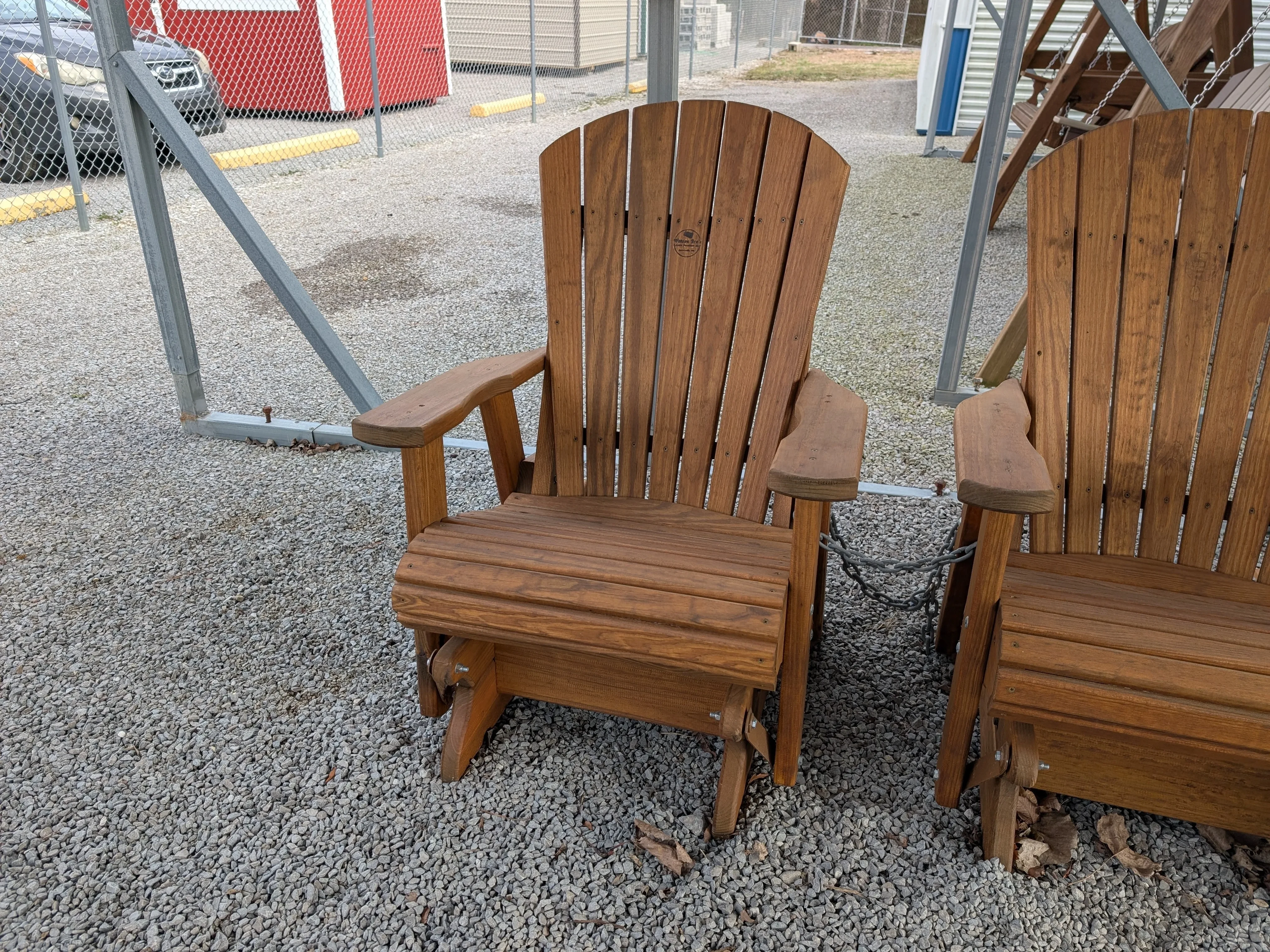 a wood chair sitting in the gravel. It can glide back and forth and is sitting next to another chair.