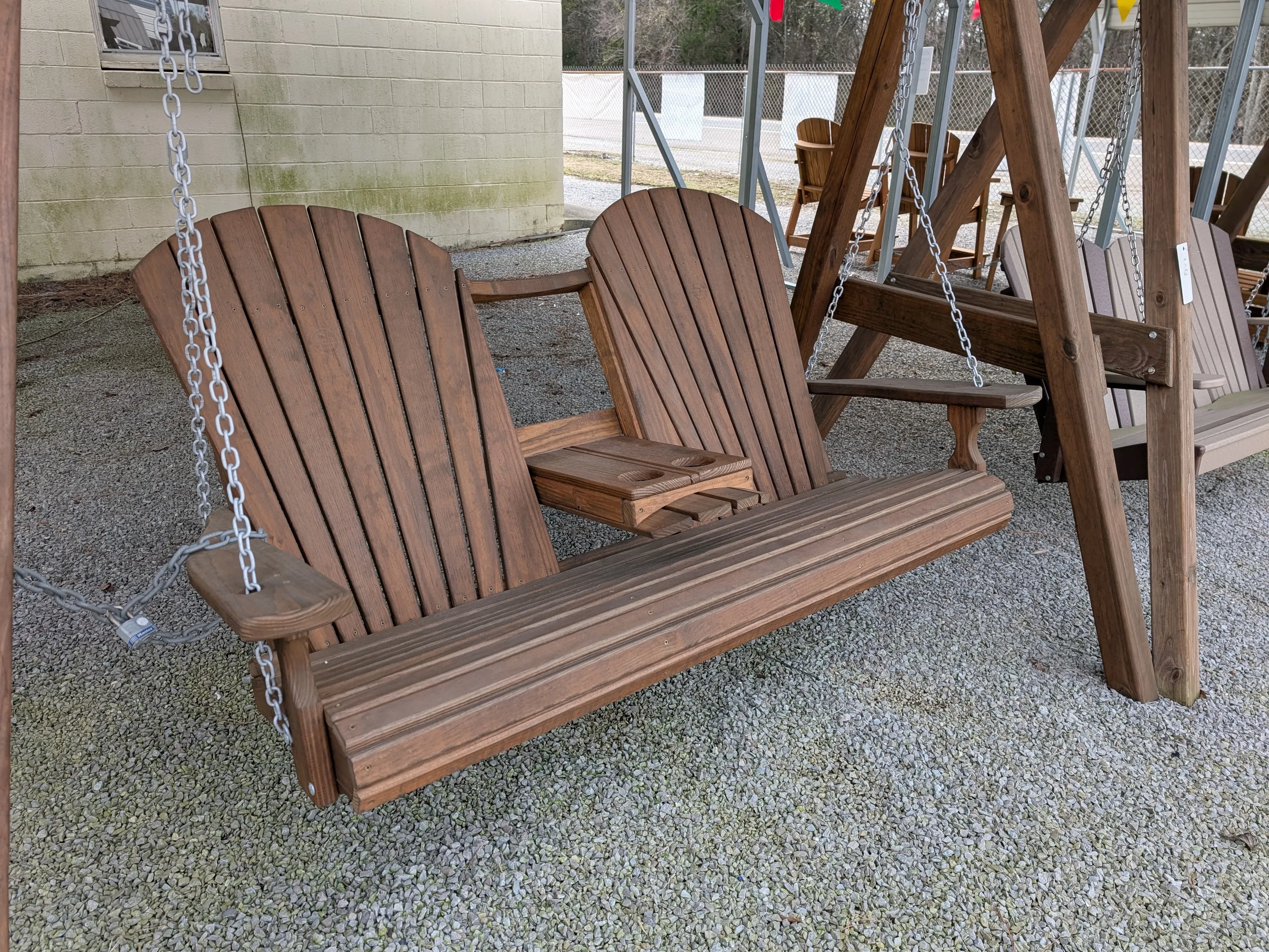 a stained and sealed wood bench swing, it has a center console in the down position and is sitting over gravel