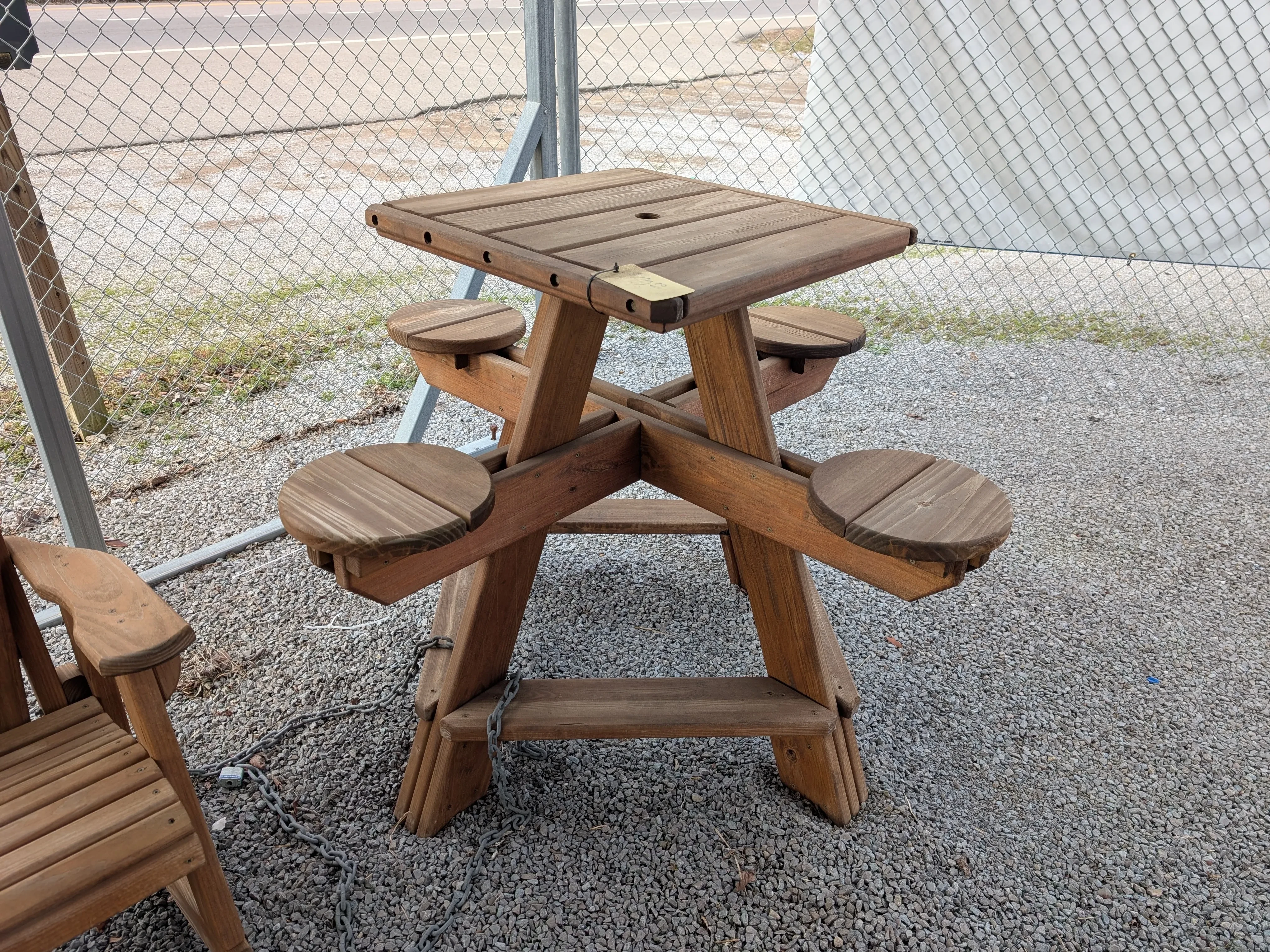 a wood table with a square tabletop. The seats are circular. It's sitting in the gravel