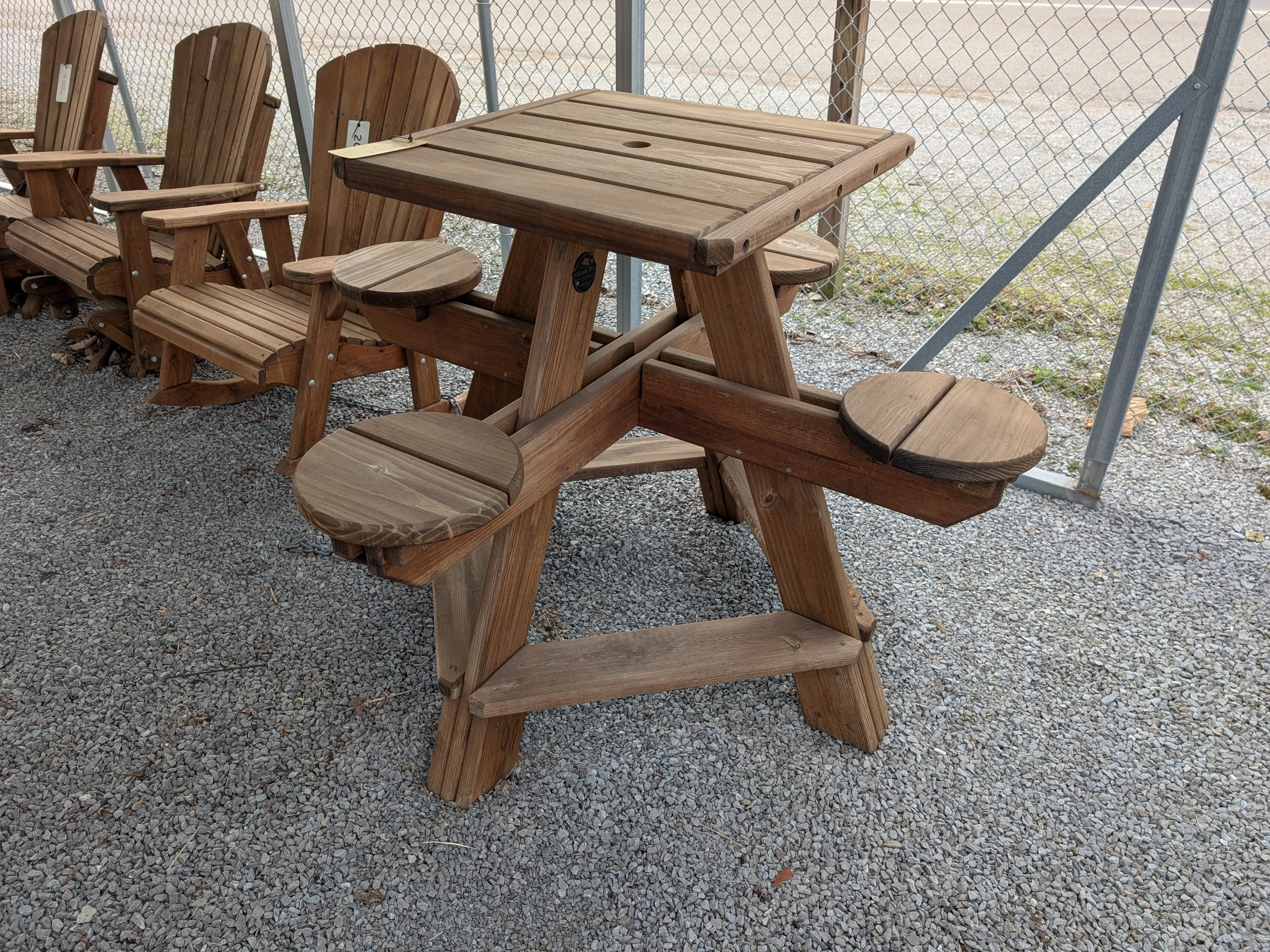 a table sitting in the gravel. The tabletop is square and the seats are circular