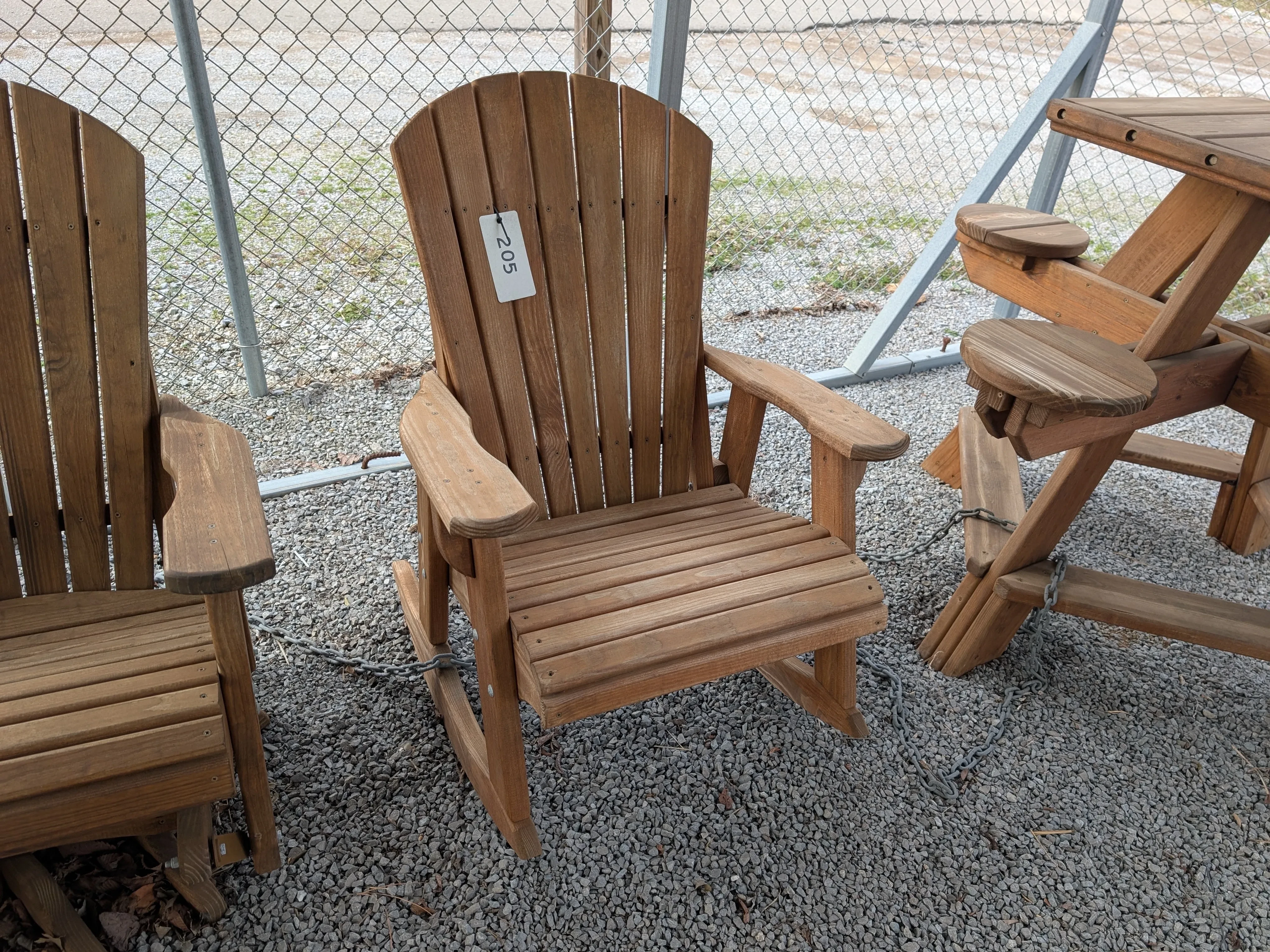 a stained and sealed wood rocking chair sitting in the gravel.