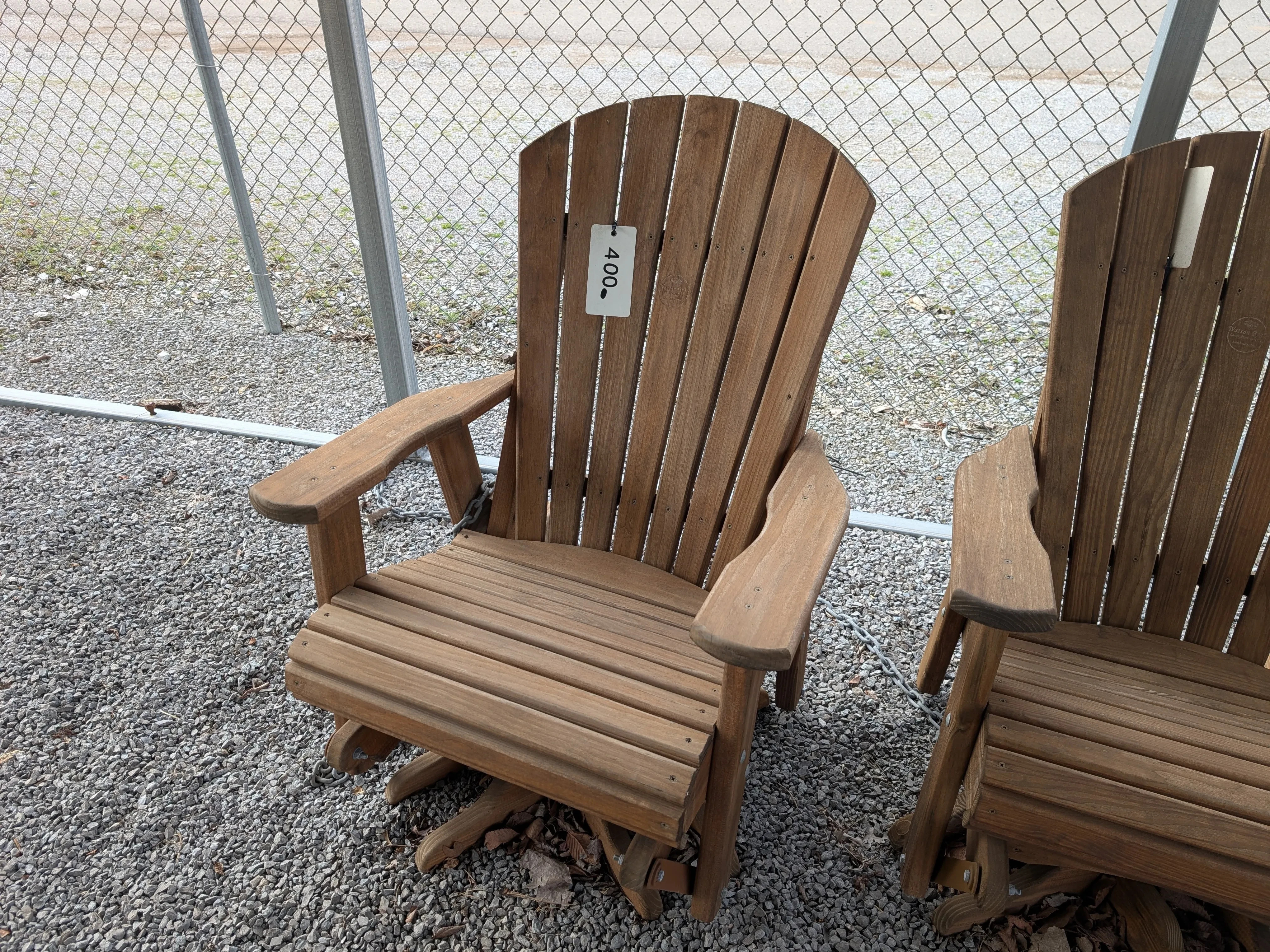a wood chair in the gravel. It has a price tag on it. It can swivel around and glide back and forth