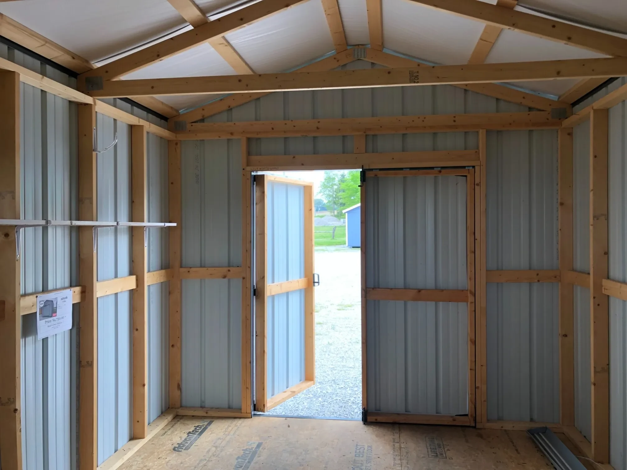 The inside of a metal shed showing the framing looking towards the doors doors which are open.