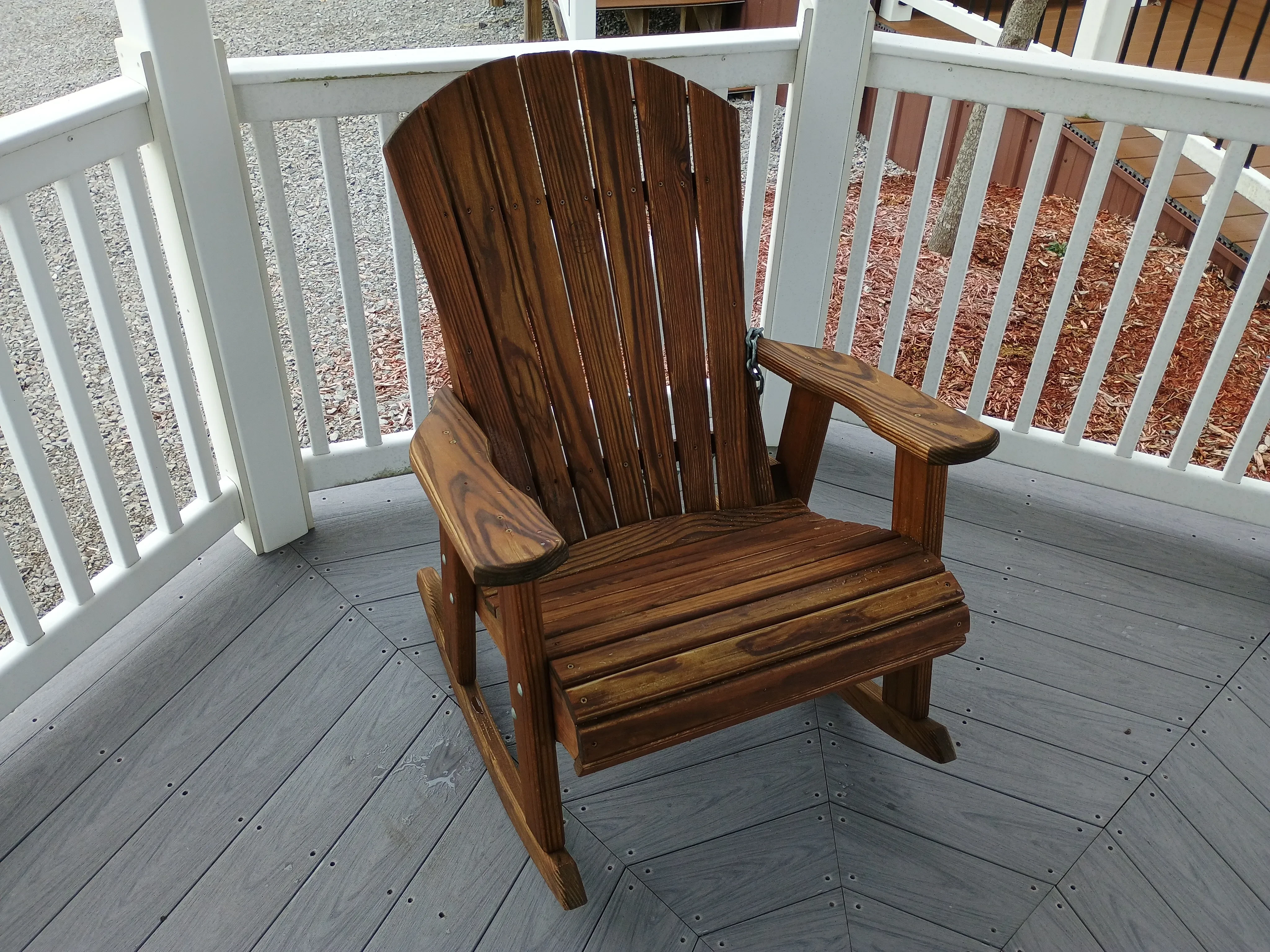 the front view of a wood stained and sealed rocking chair. It is inside of a white gazebo with gray vinyl flooring