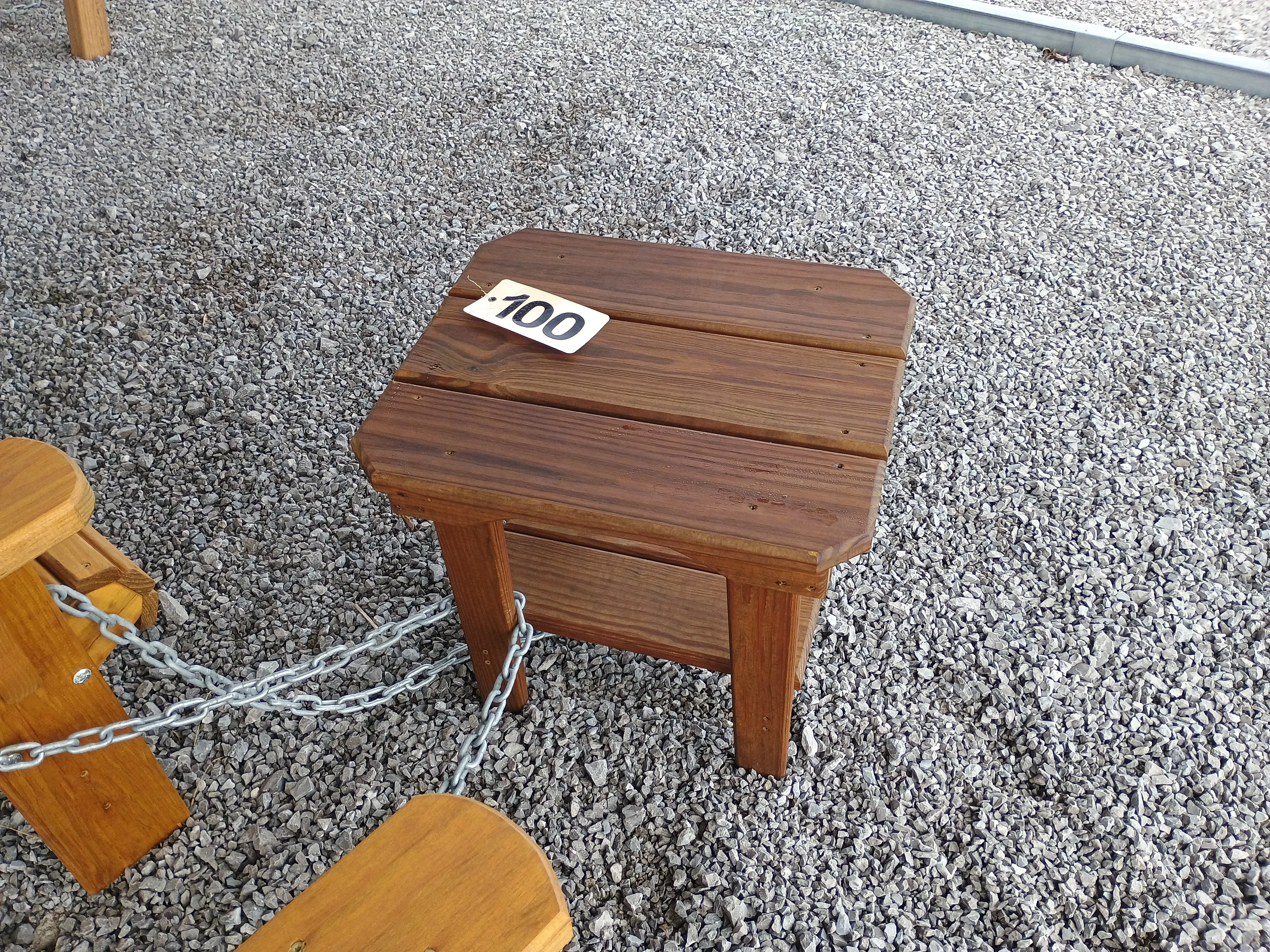 a stained and sealed wood table sitting in the gravel. It is chained up to other furniture