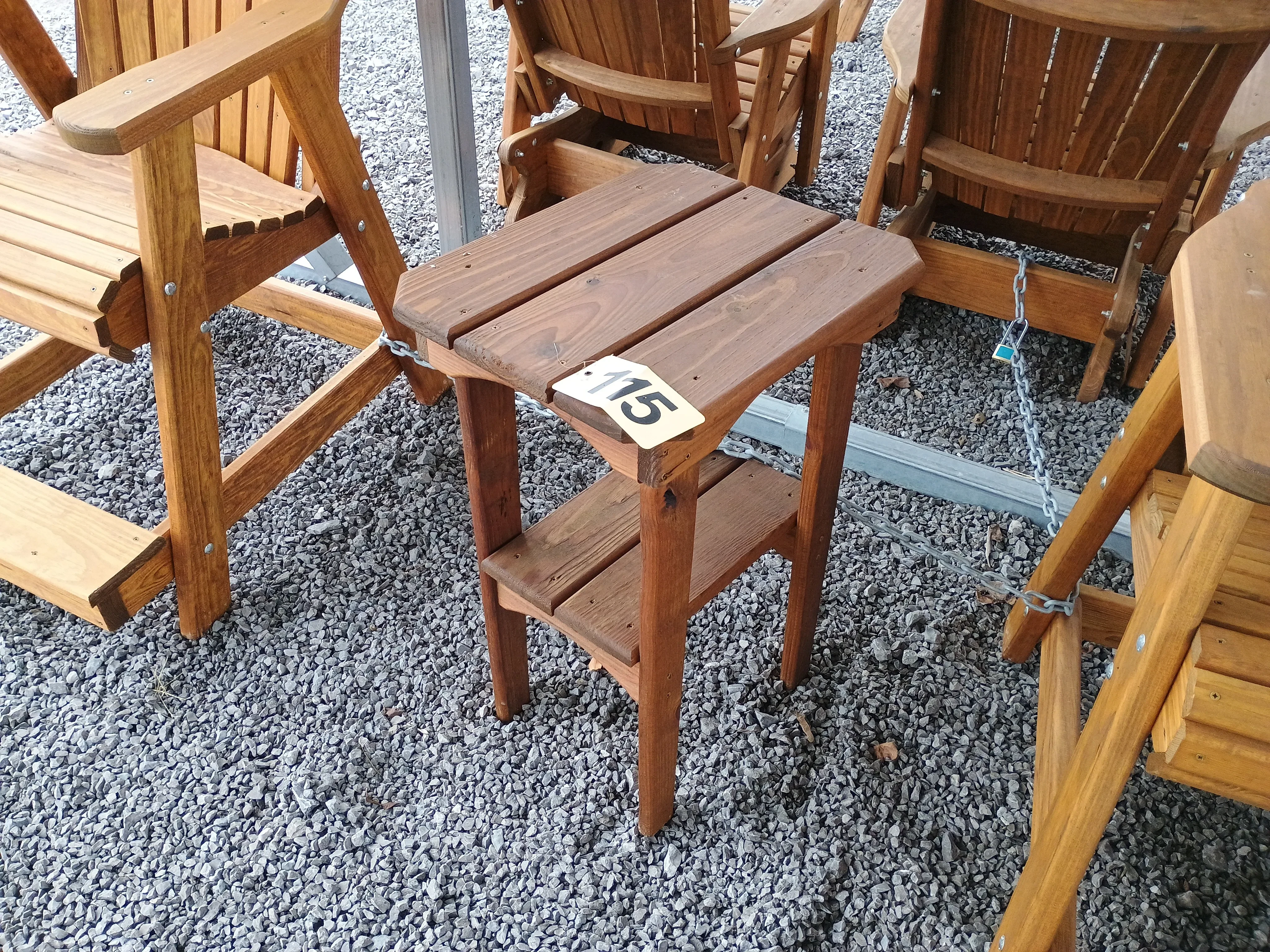 a wood table sitting in the gravel. It has a yellow price tag on it that shows "115".
