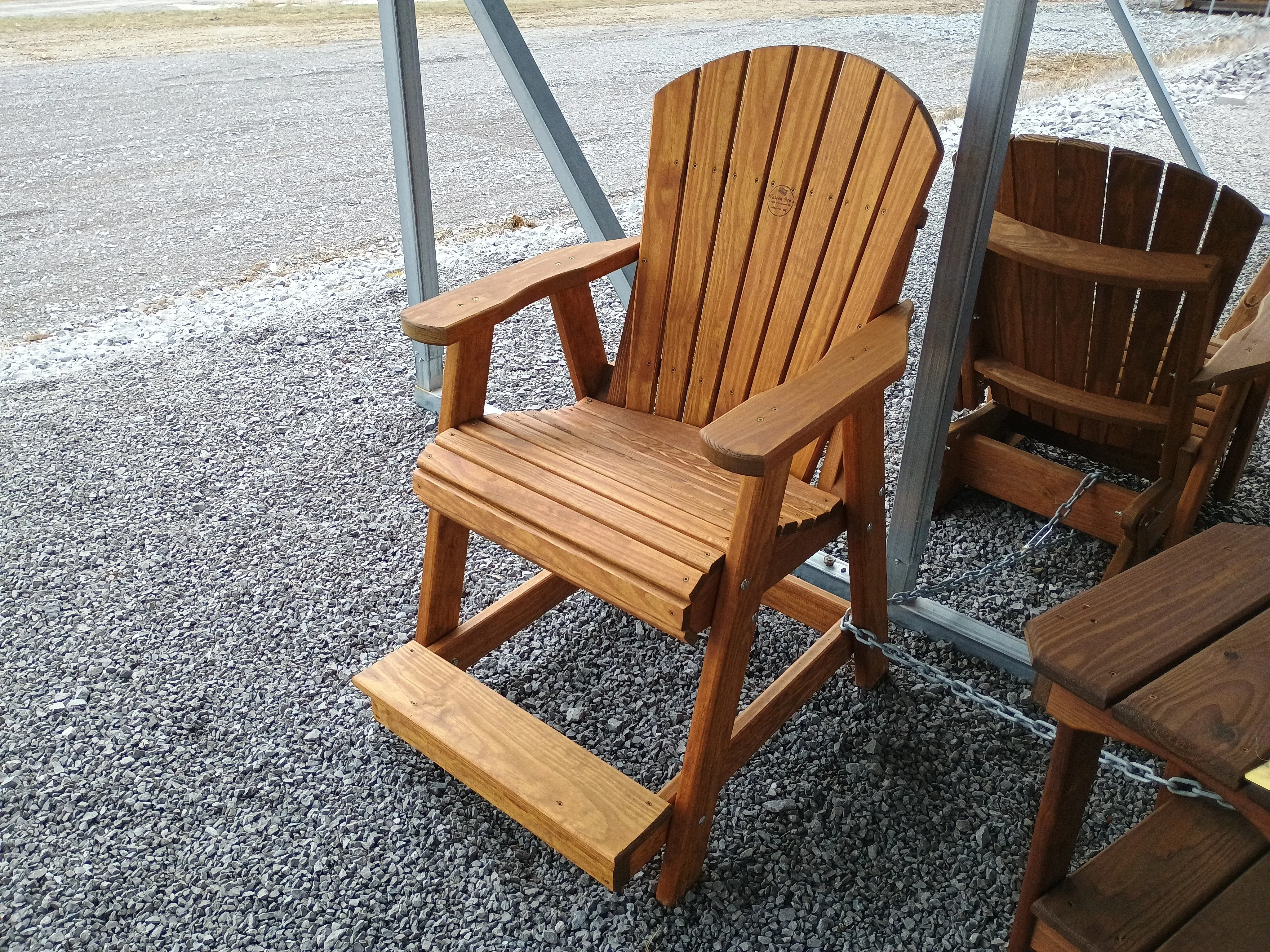 a wood stained and sealed chair sitting in the gravel. It has armrests and footrests