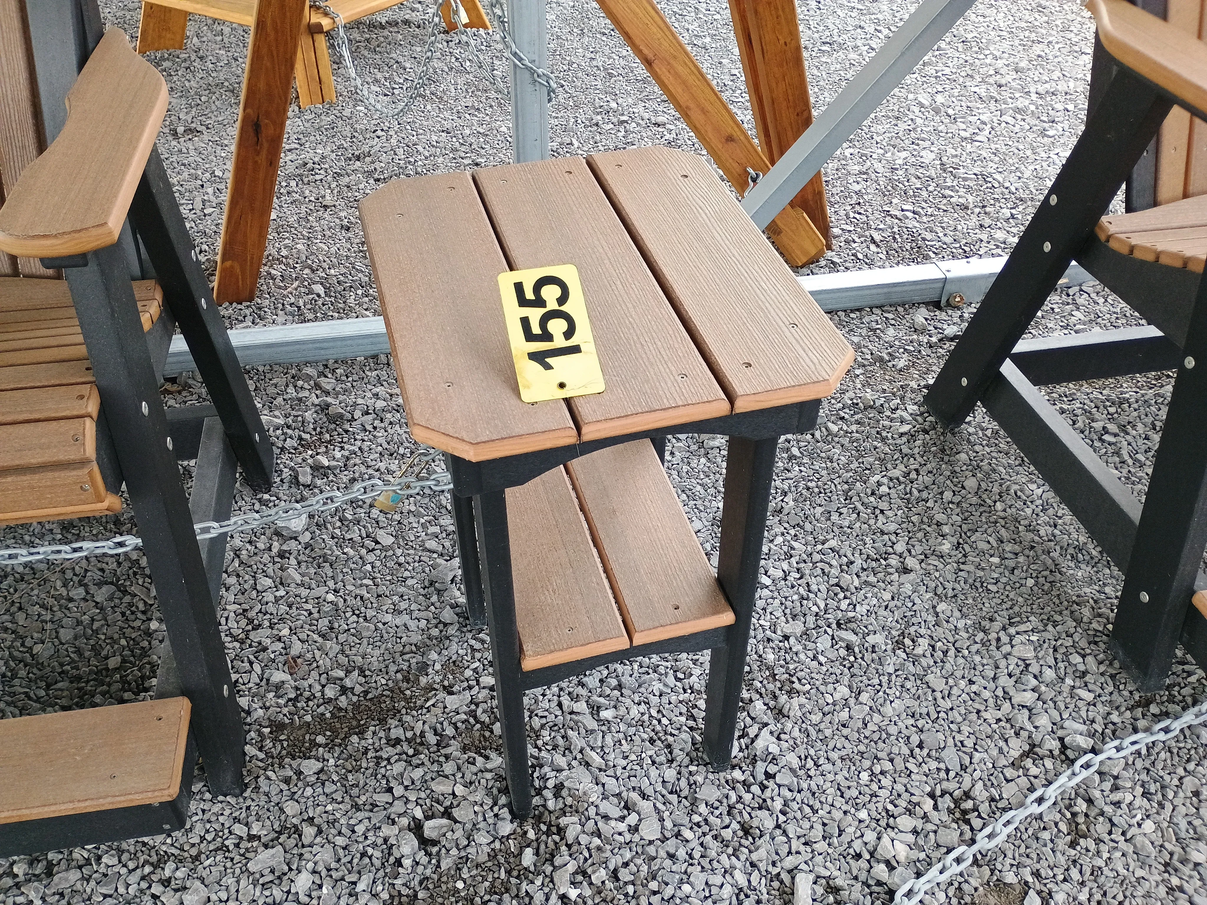 a table sitting in the gravel. It has a tabletop and a smaller one underneath. It has black legs and brown tabletops