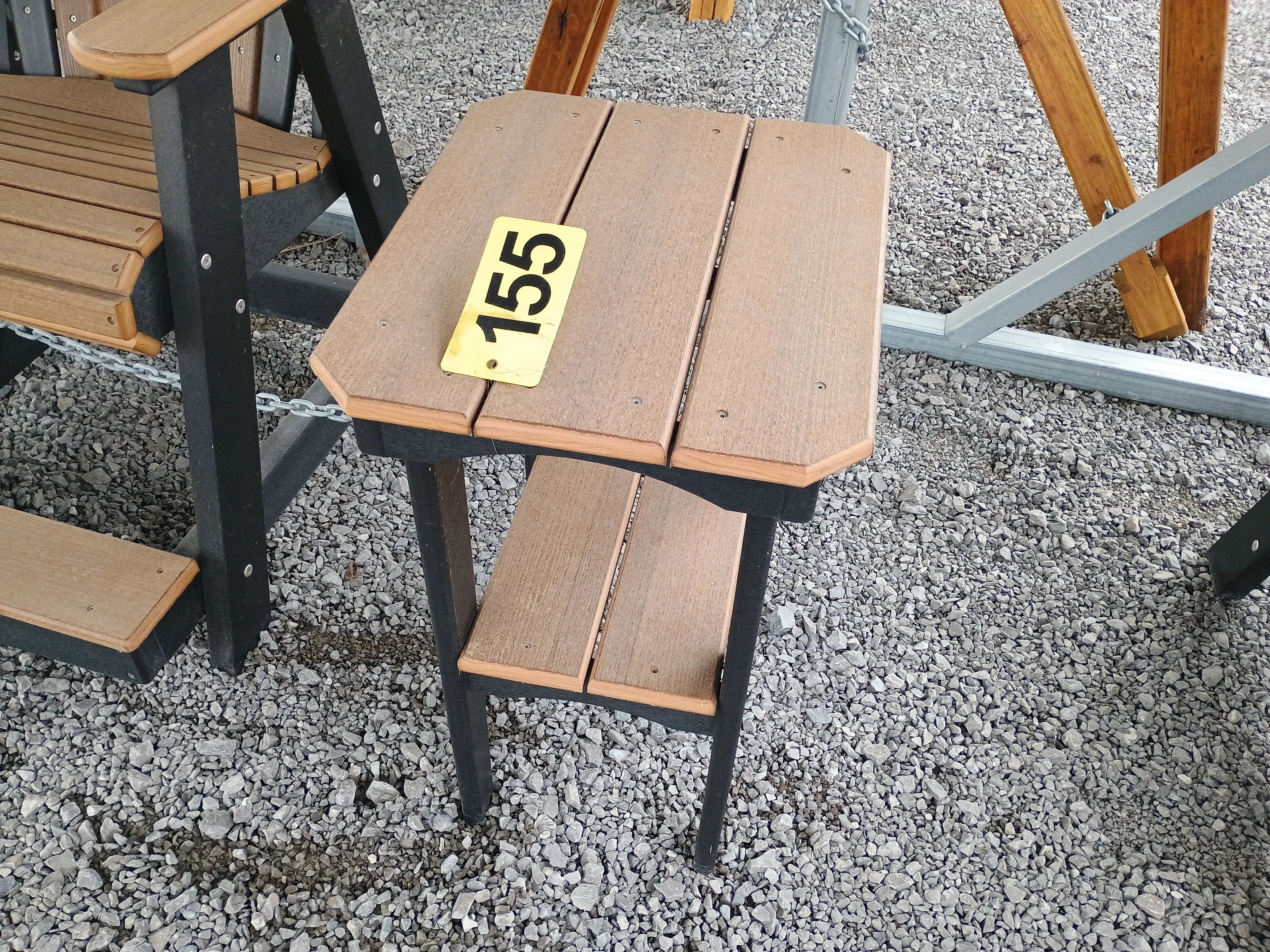 a table with black legs and brown tabletop sitting in the gravel. It has a yellow price tag that shows "155"