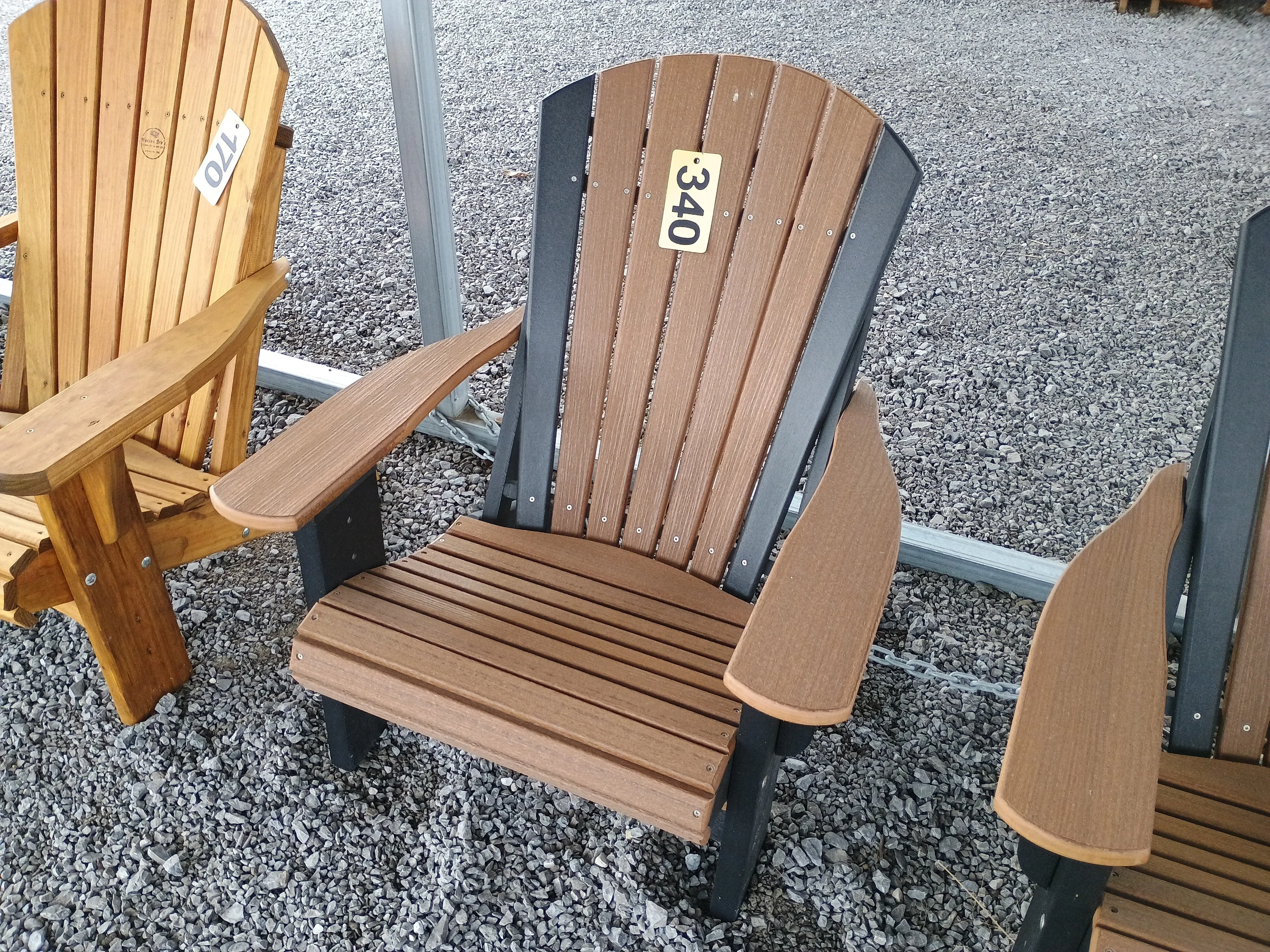 A polywood chair sitting in the gravel. It has other chairs next to it. It is black and brown