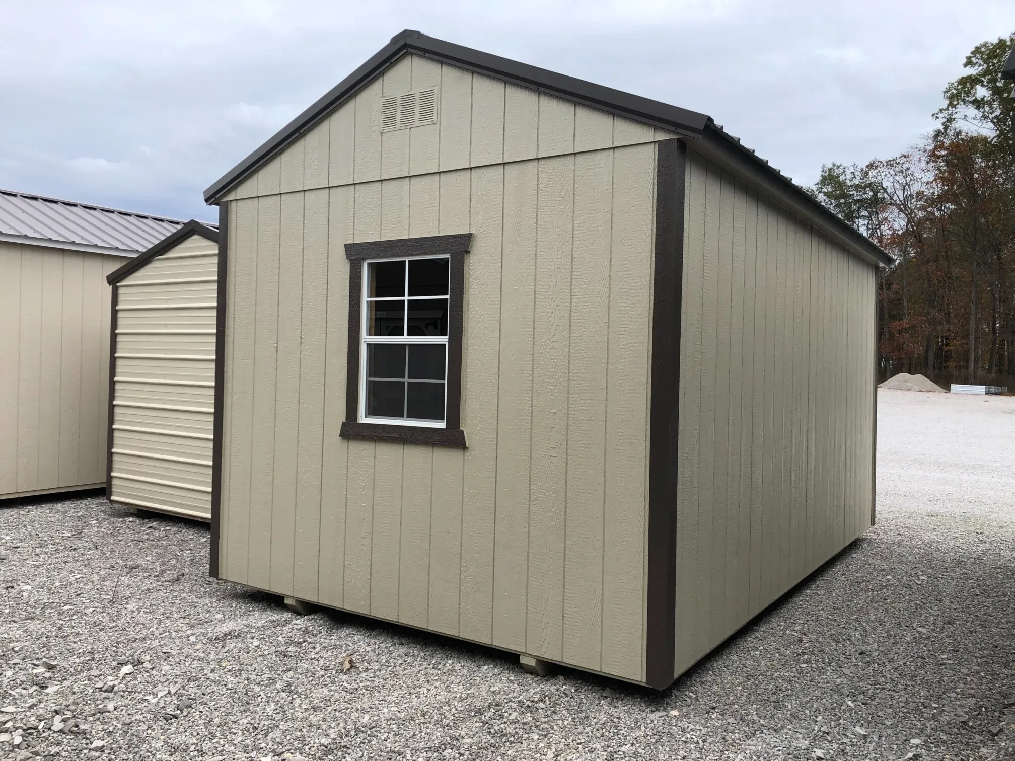 the rear corner view of a light stone colored shed showing a window in the middle of the back wall