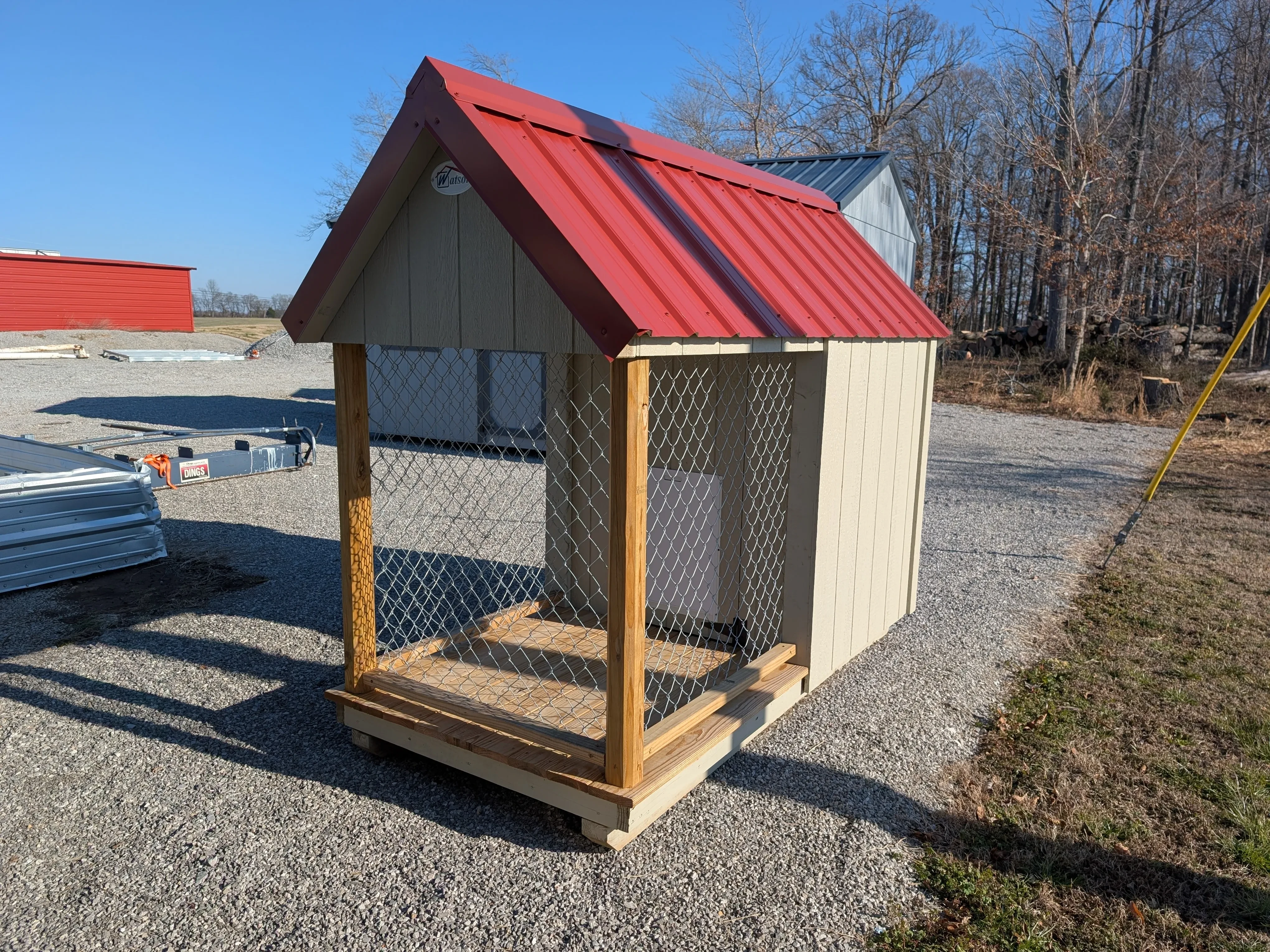 a dog kennel with a chain-link run. It has a red roof and is sitting on gravel