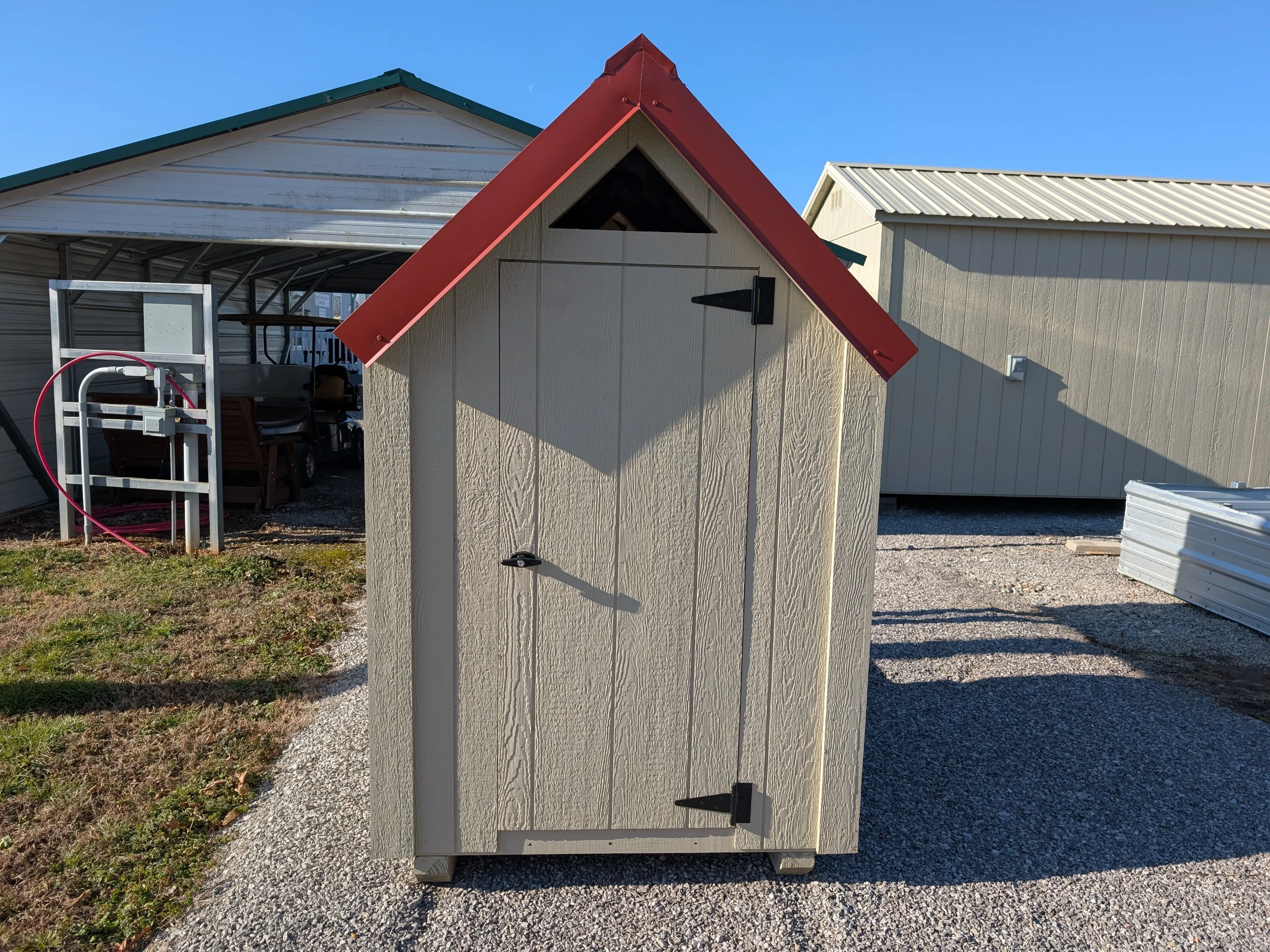 the back of a dog kennel. It shows a man door with a triangle shaped vent. It also has a red metal roof