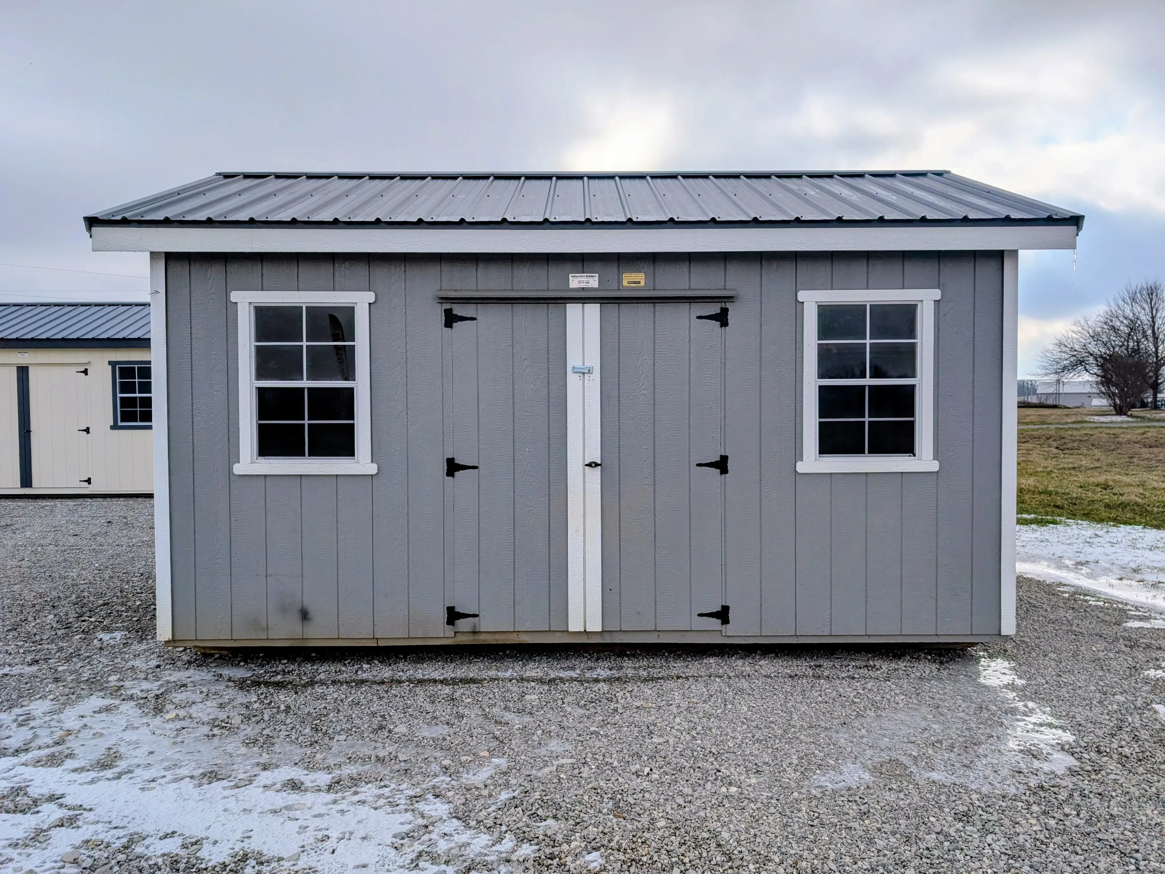 the front view of a gray shed with white trim. It has two windows and double doors