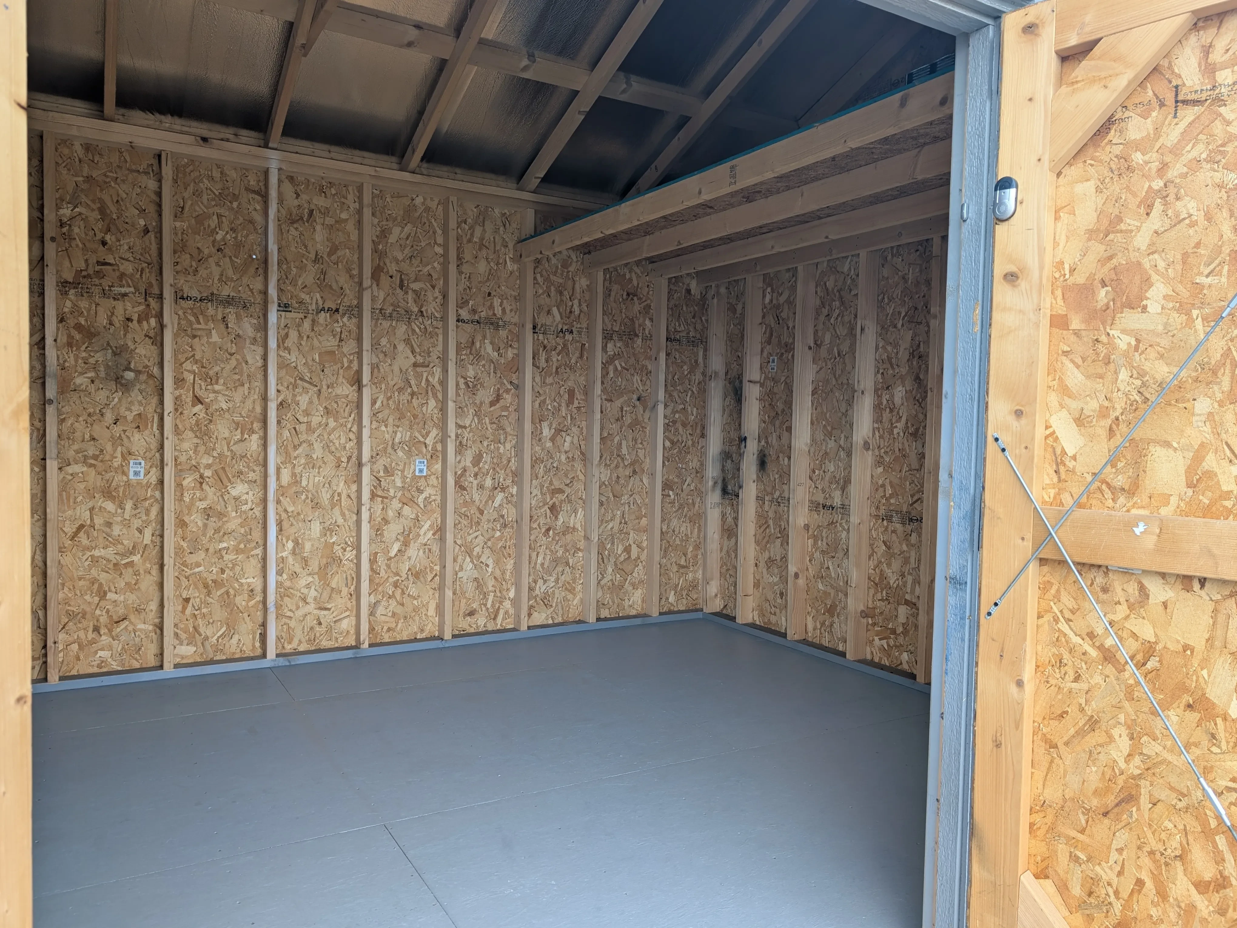 the inside of a wood garden shed. There is a loft and the floor is painted gray