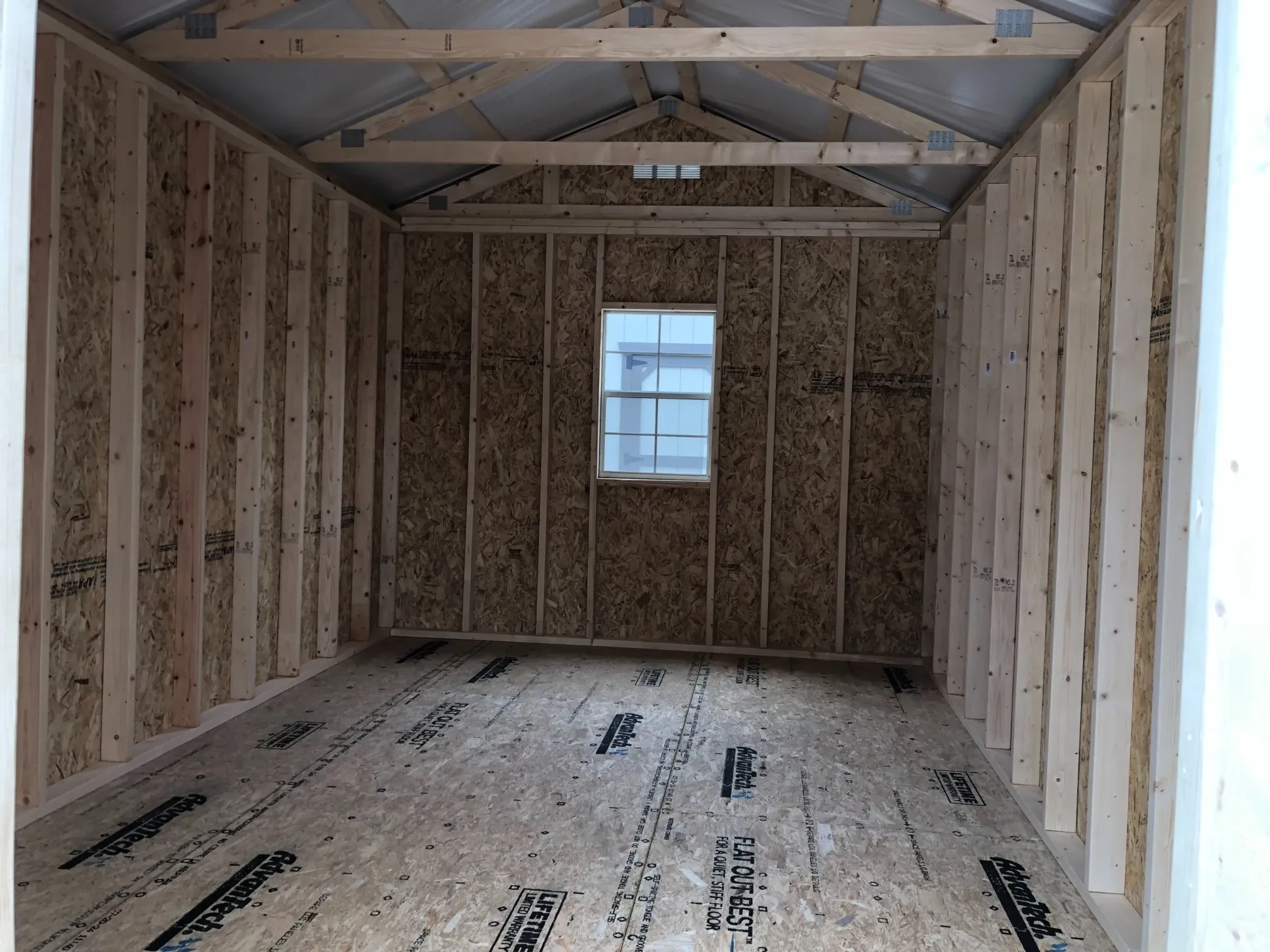 The inside of a wood shed showing the floor, frame, and a window on the back wall