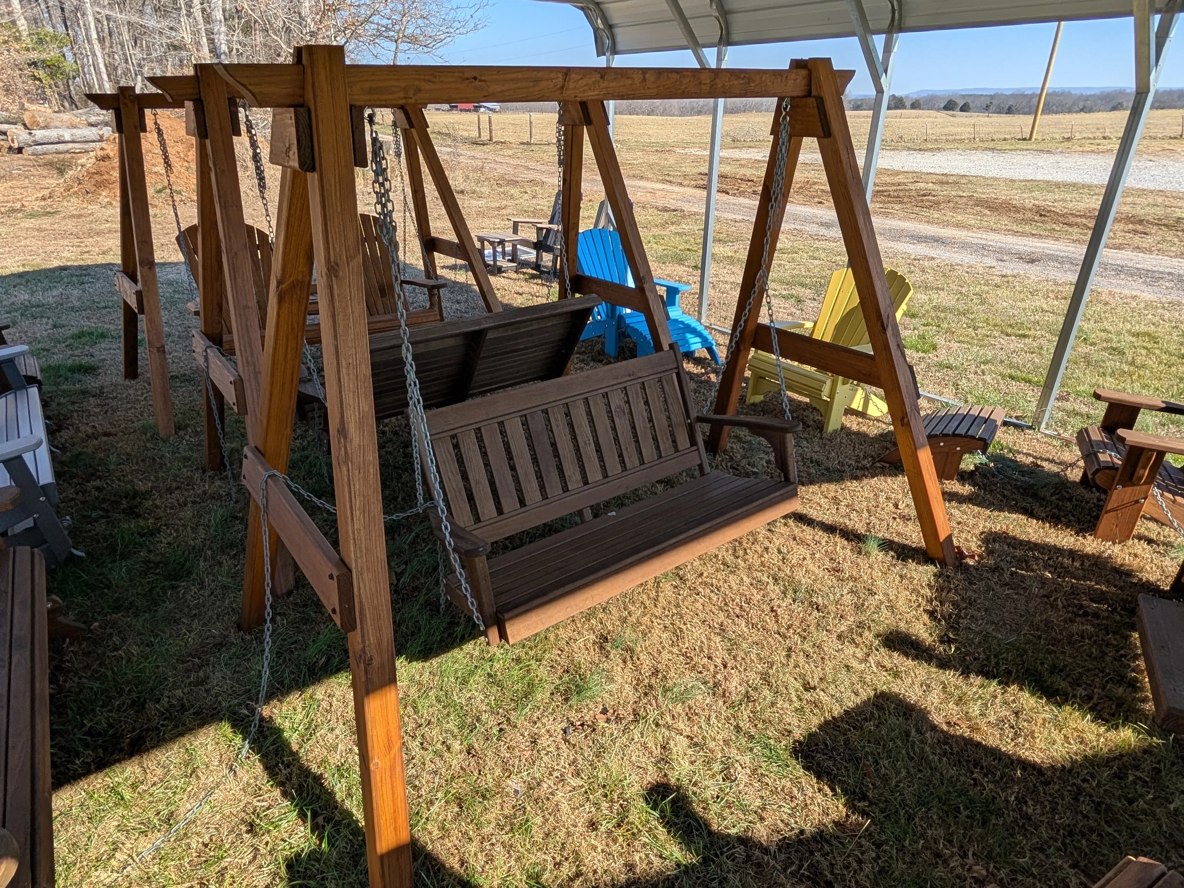 a garden swing held up by an a-frame wooden structure in the grass near other furniture
