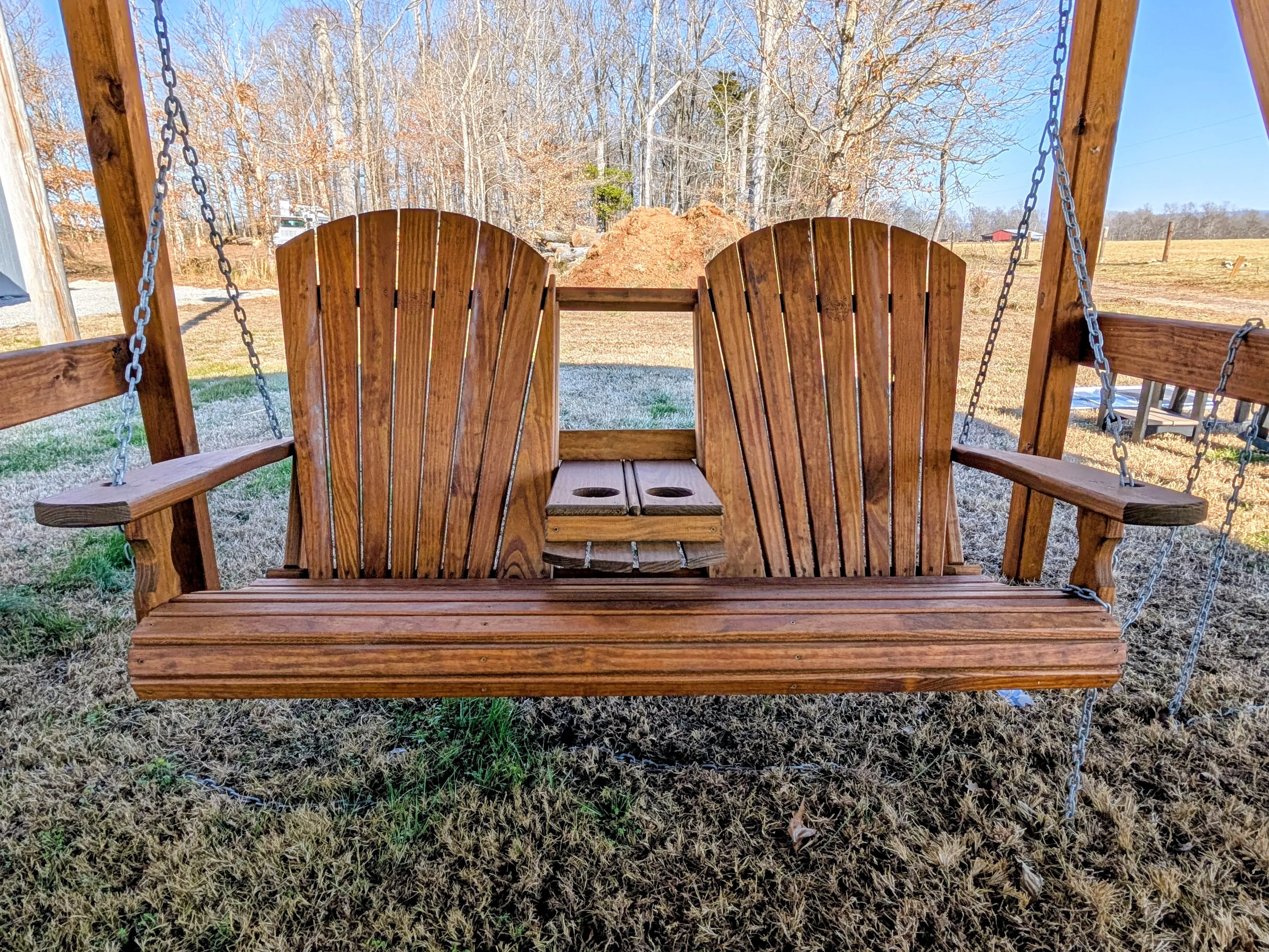 a wood swing with a center console with cupholders in the down position. It's sitting in the grass