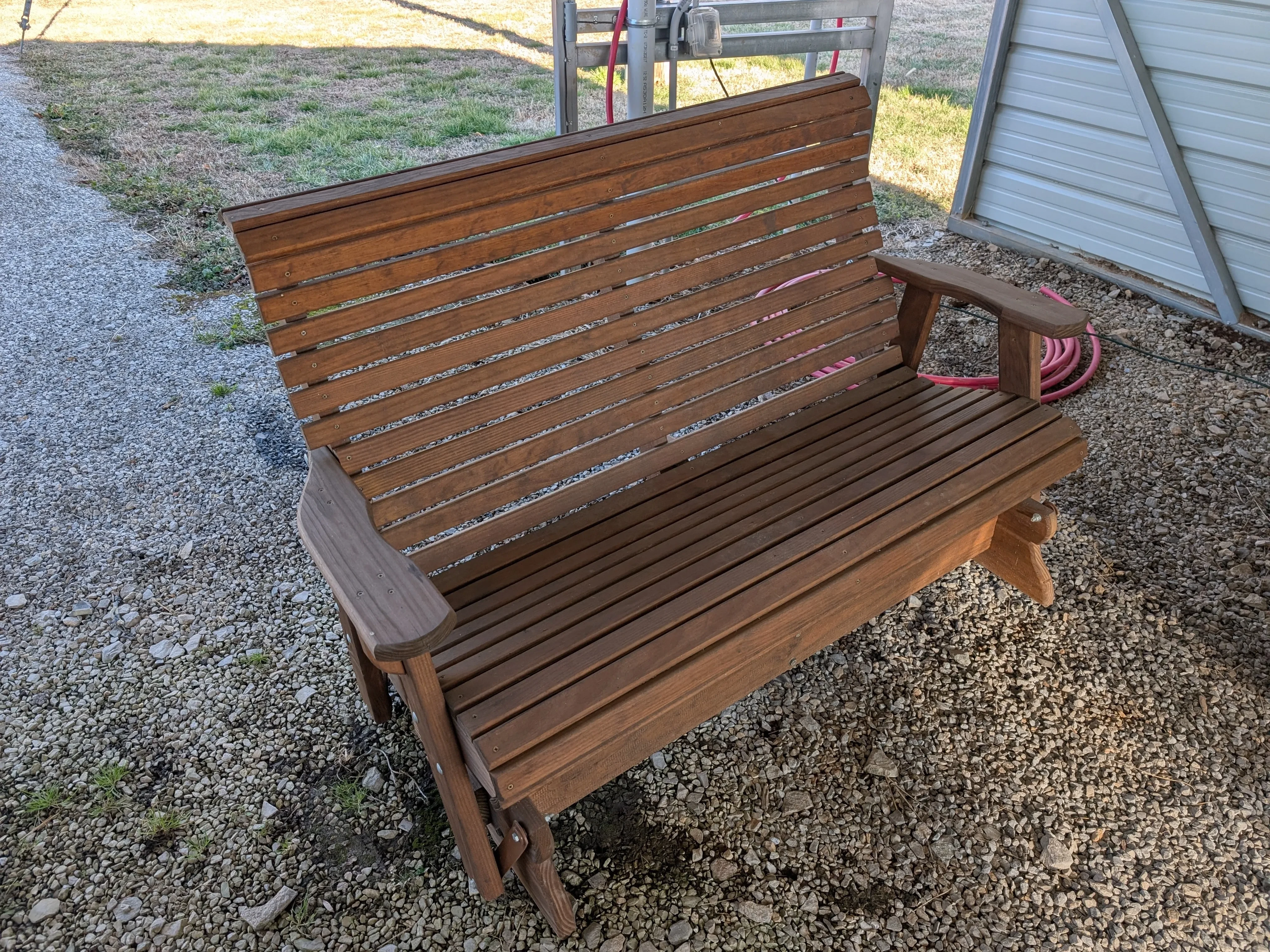 a wood stained and sealed bench sitting under a carport. it is about 5 feet long