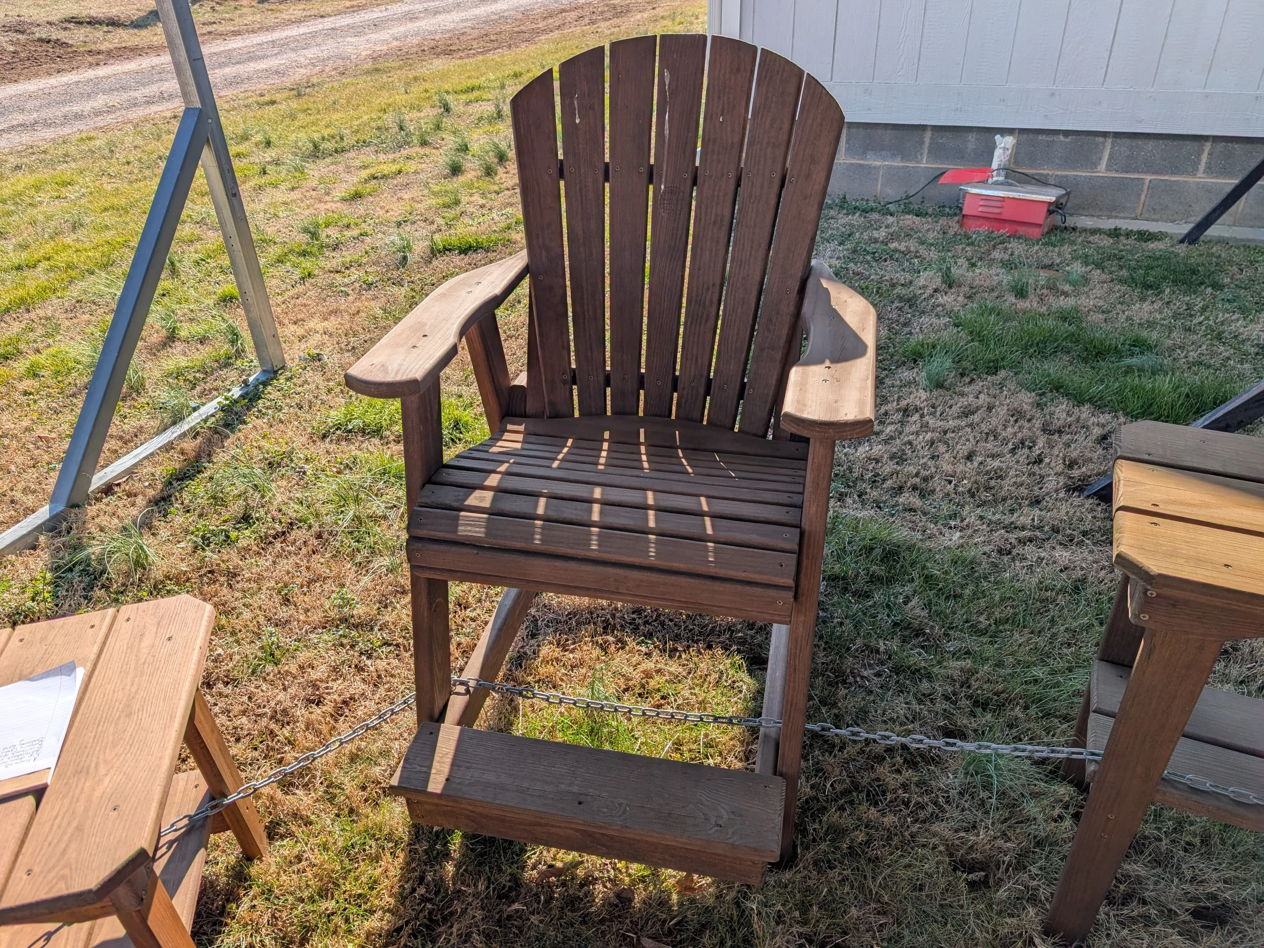 a wood stained and sealed chair sitting in the shade. It has arm and foot rests