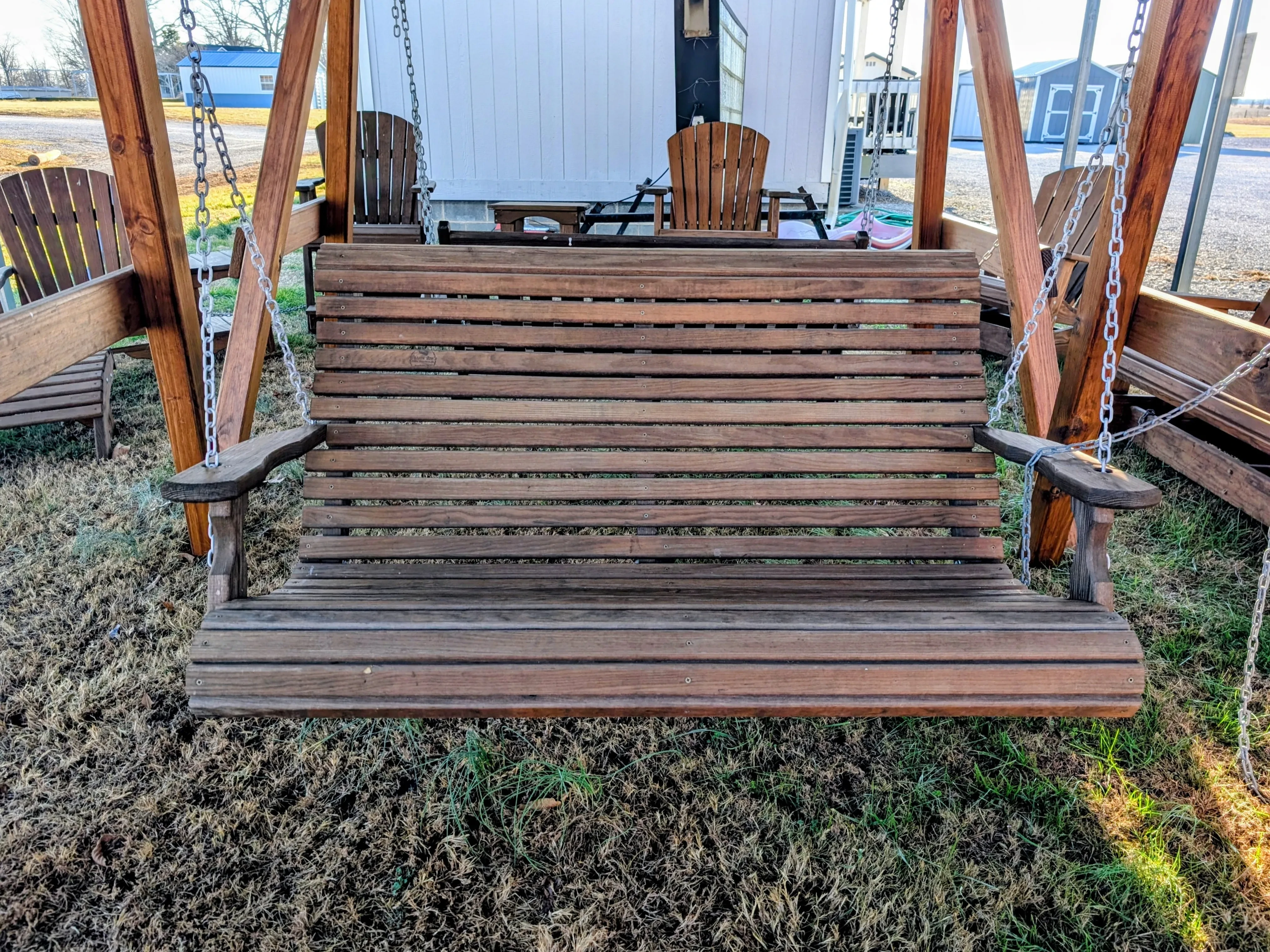 a wood stained and sealed bench being held up by chains in the grass