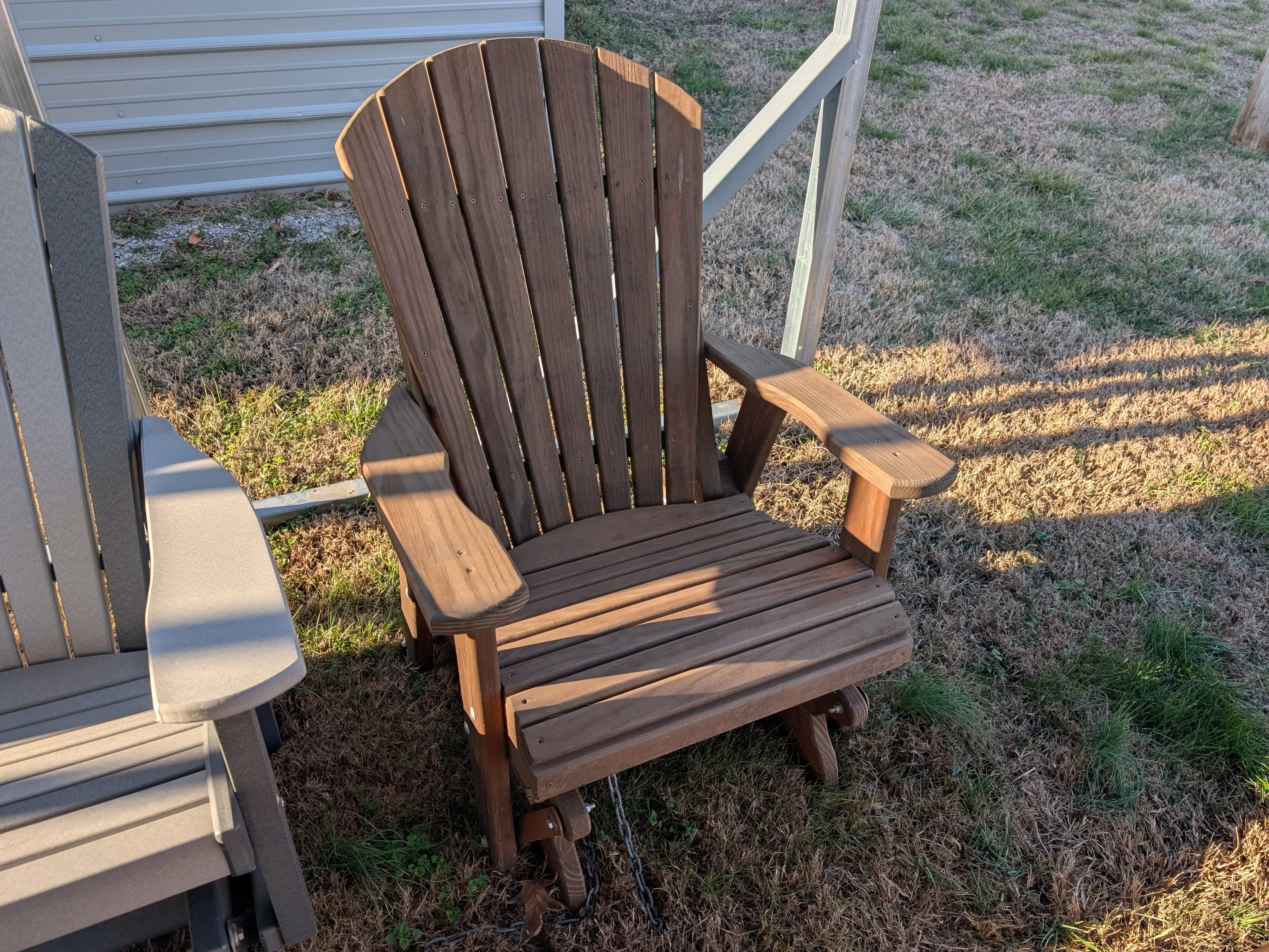 a wood stained and sealed chair that can glide back and forth. It is sitting in the grass