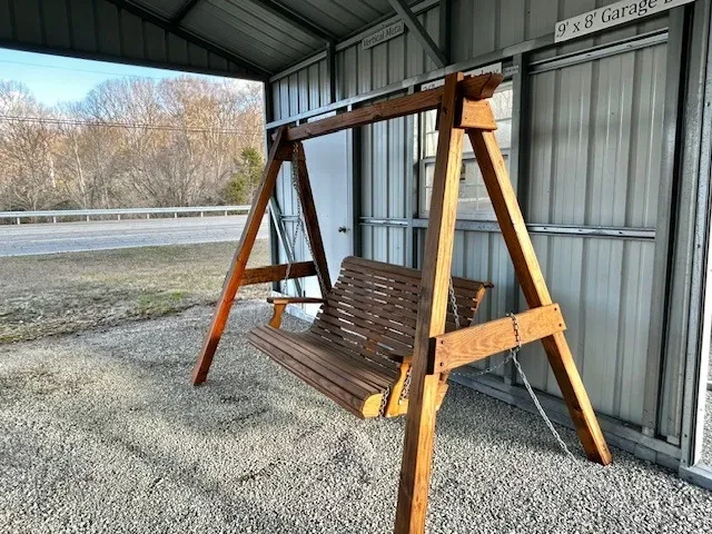 the side view of a wood swing under a carport. It is held up by a wood a-frame structure