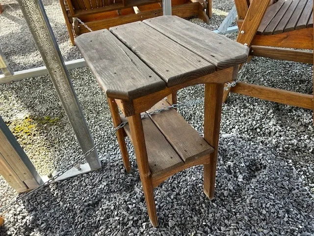 a wood stained and sealed table sitting in the gravel. It is chained up to other furniture
