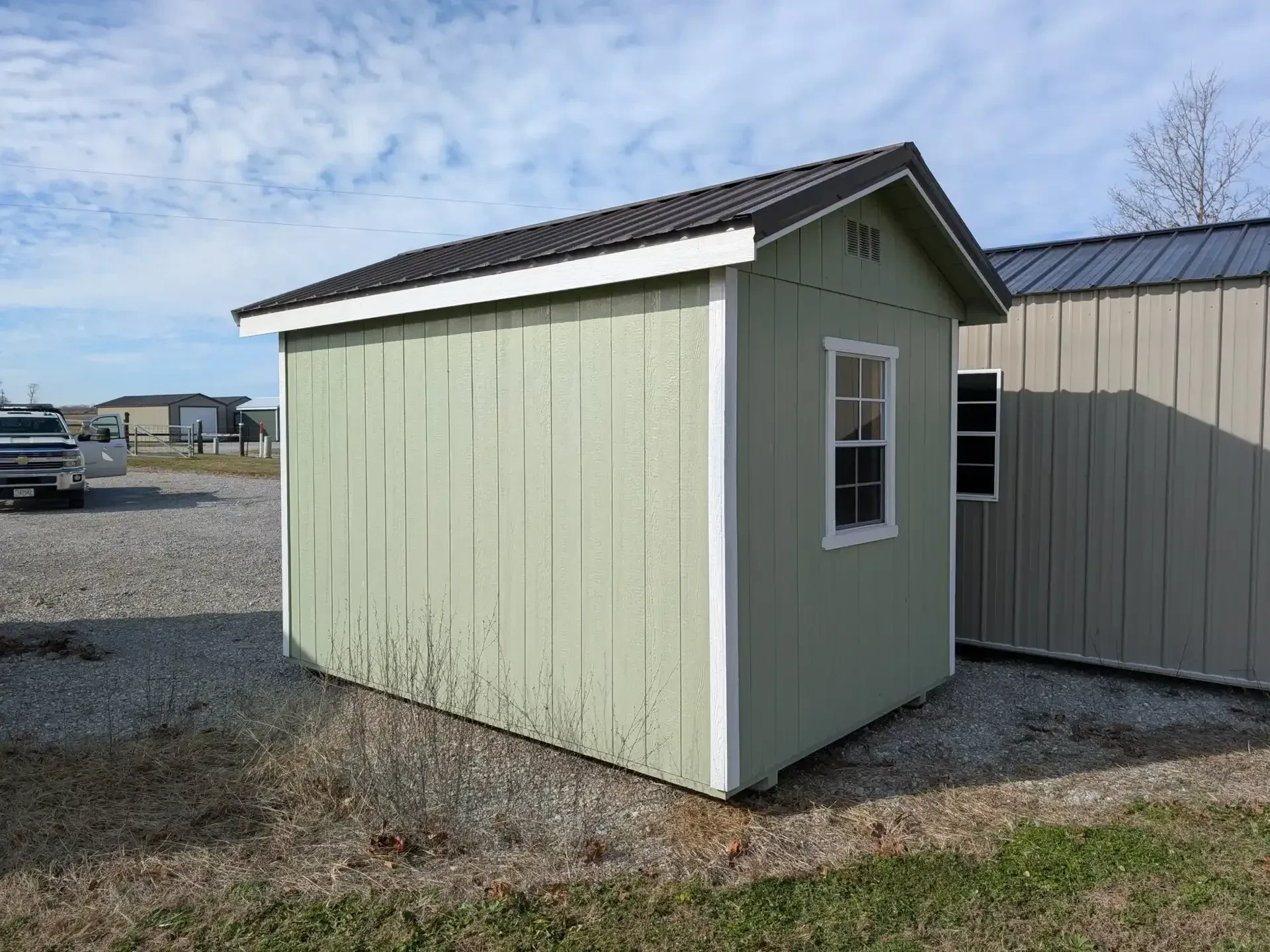 The rear view of a light green shed showing a window in the middle of the back wall.