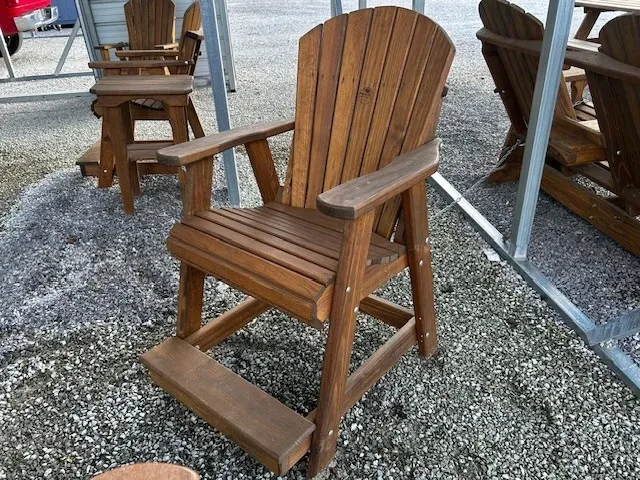 a wood stained and sealed chair with arm and foot rests. It is sitting in the gravel