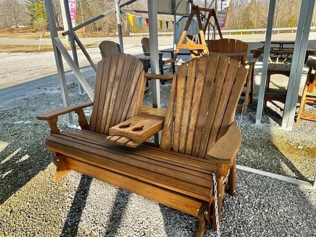a stained and sealed wood bench with two seats and a center console with cupholders. It is sitting in gravel