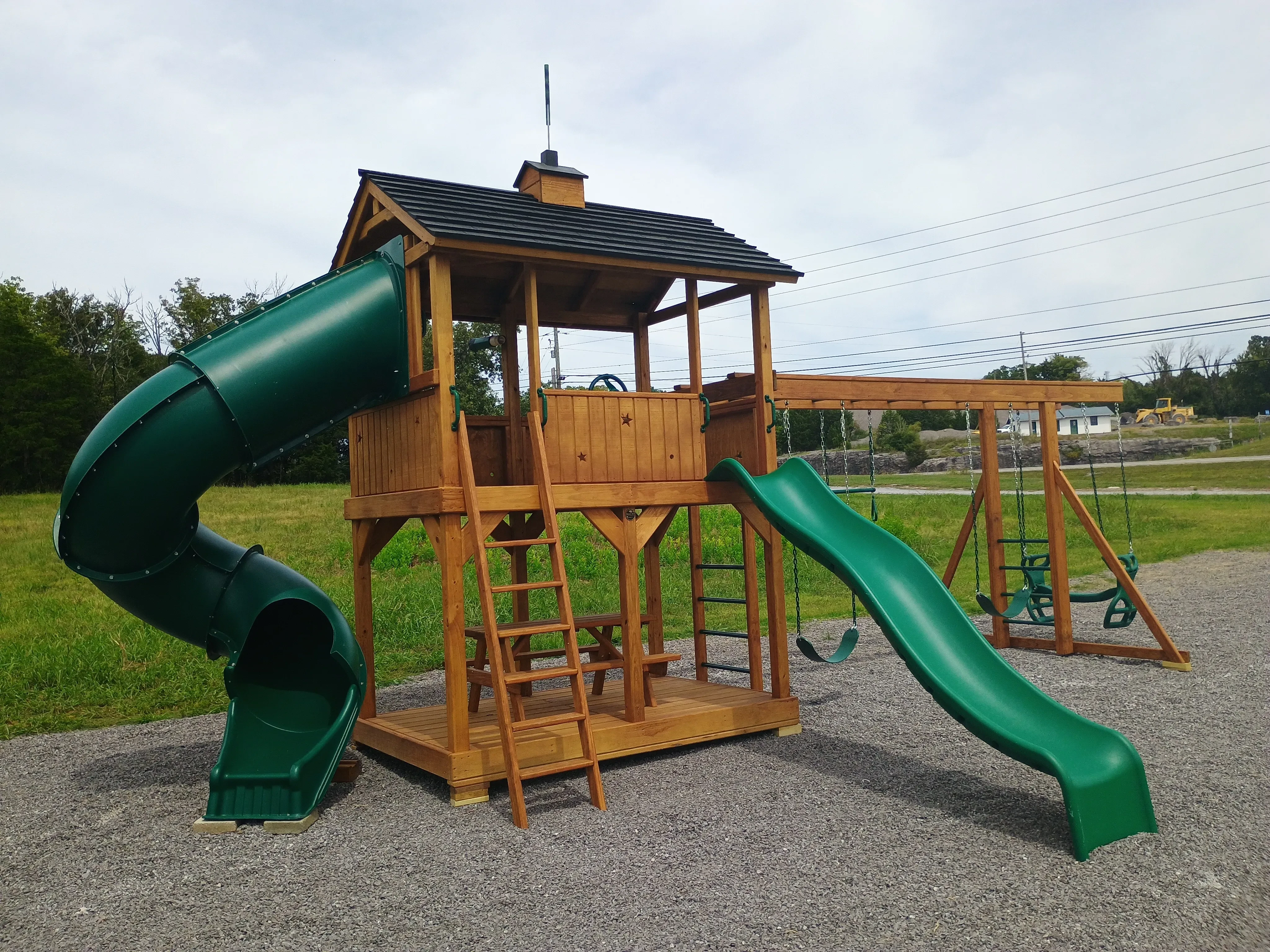 a wood stained and sealed playset. It has two green slides and a couple green swings