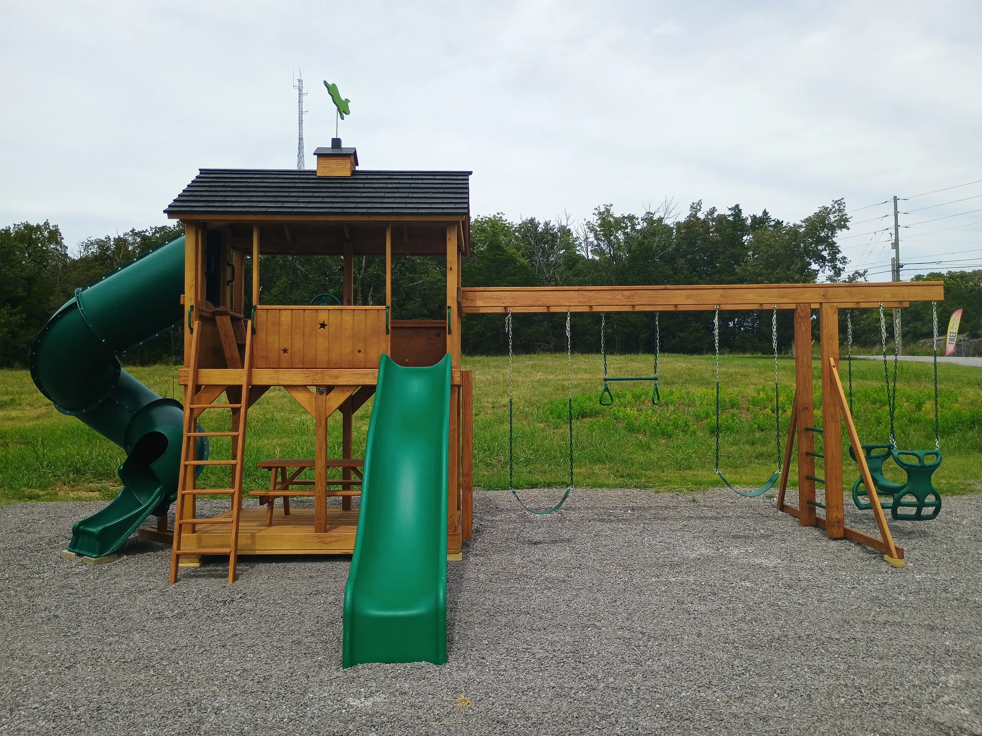 the front view of a wood playset. It has two green slides and a trapeze bar which has two green swings
