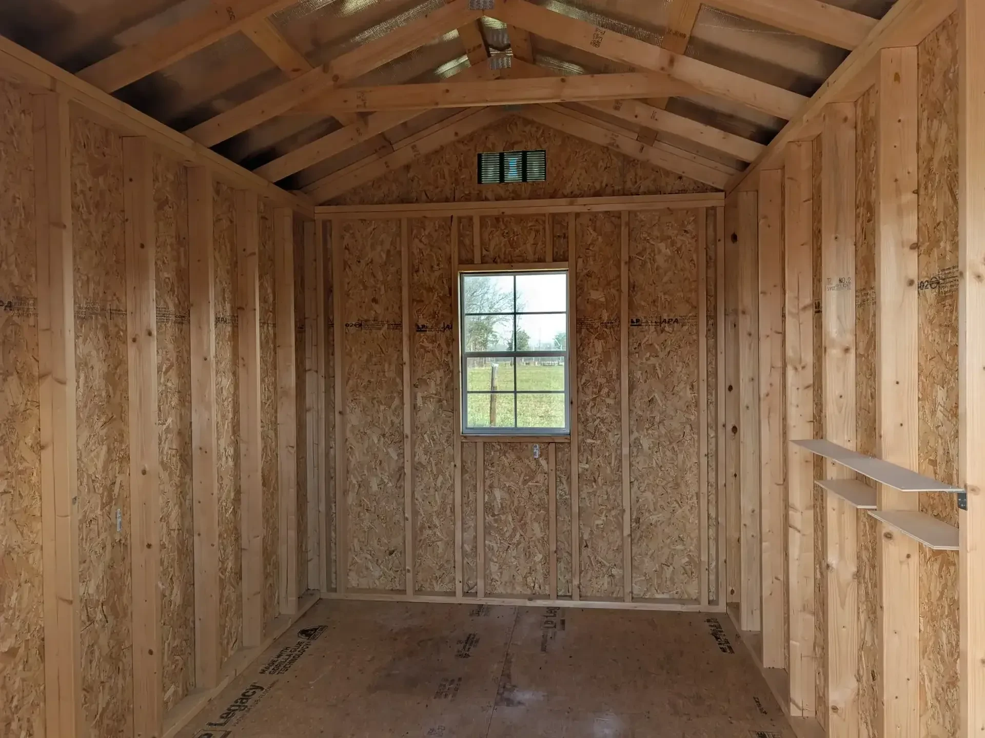 The inside of a wood shed showing a window in the middle of the back wall