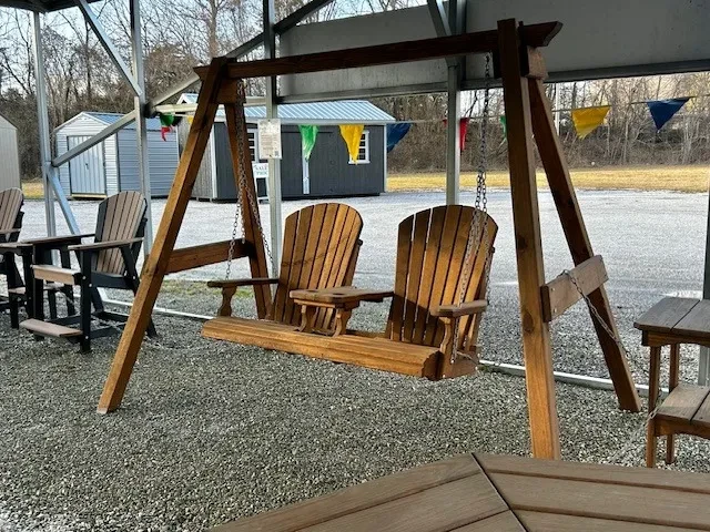 a wood swing with two seats being held up by an a-frame structure. It is under a carport
