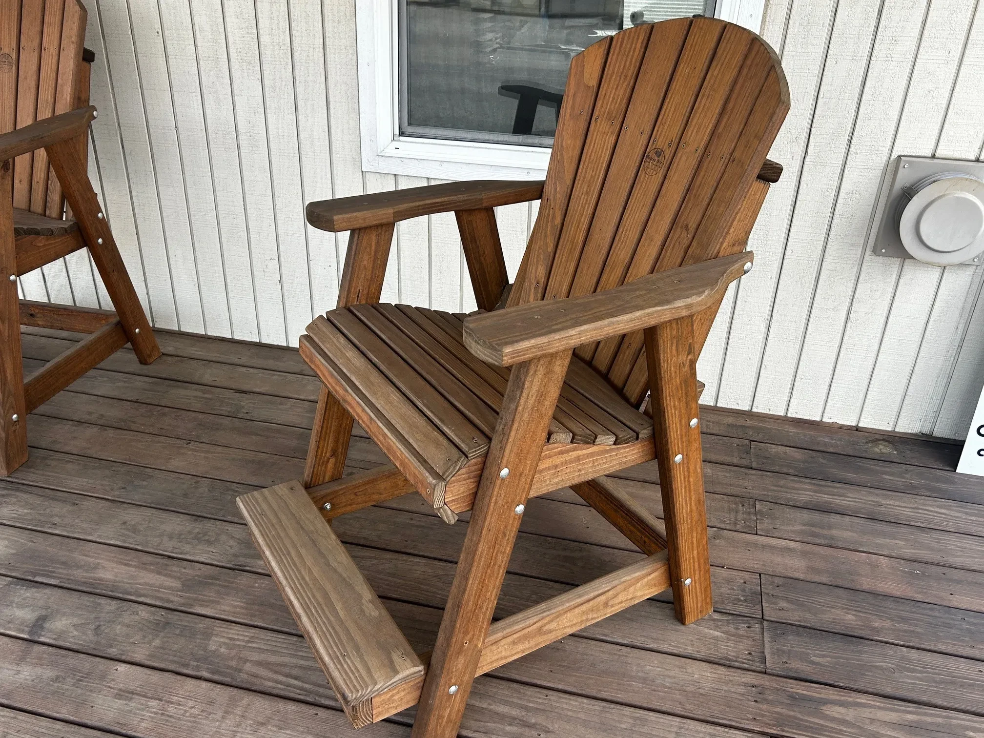 a wood chair sitting on a porch. It has armrests and footrests