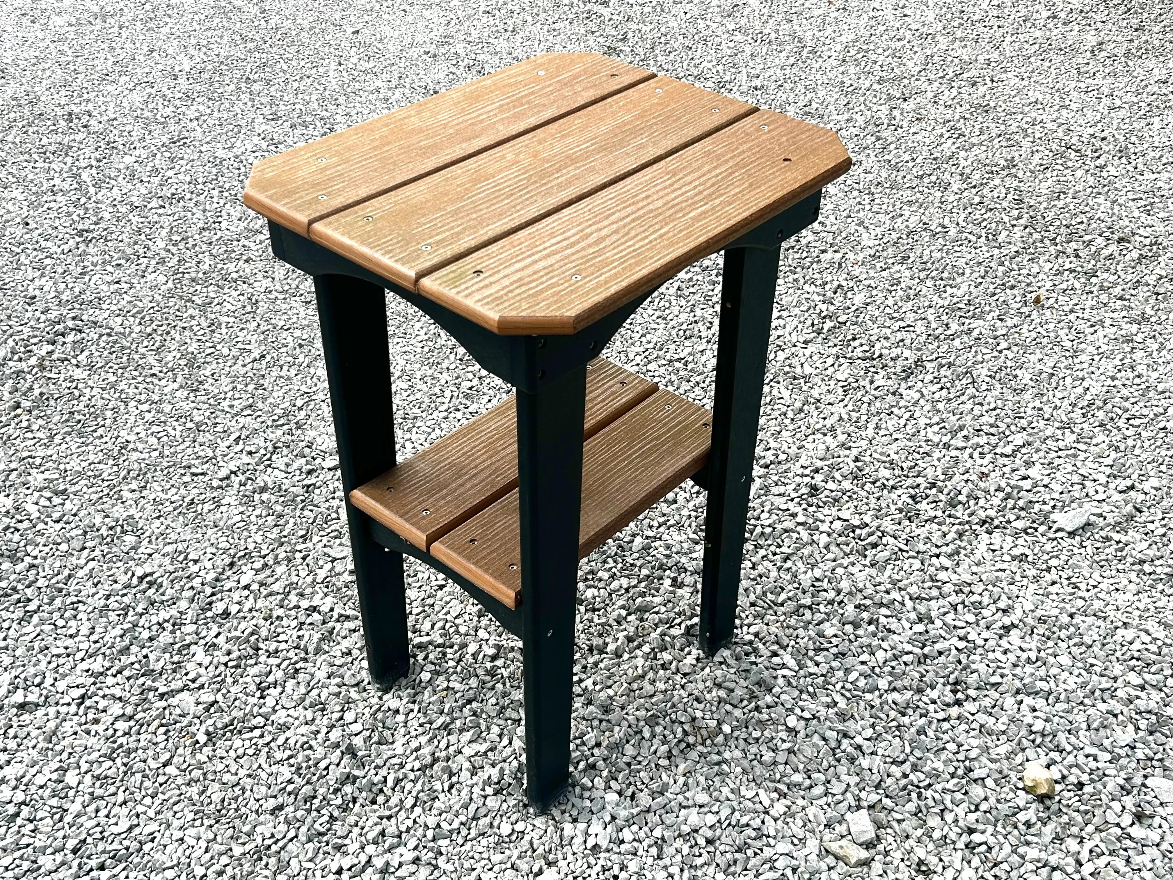a brown and black table sitting in the gravel. It is made of a polywood material