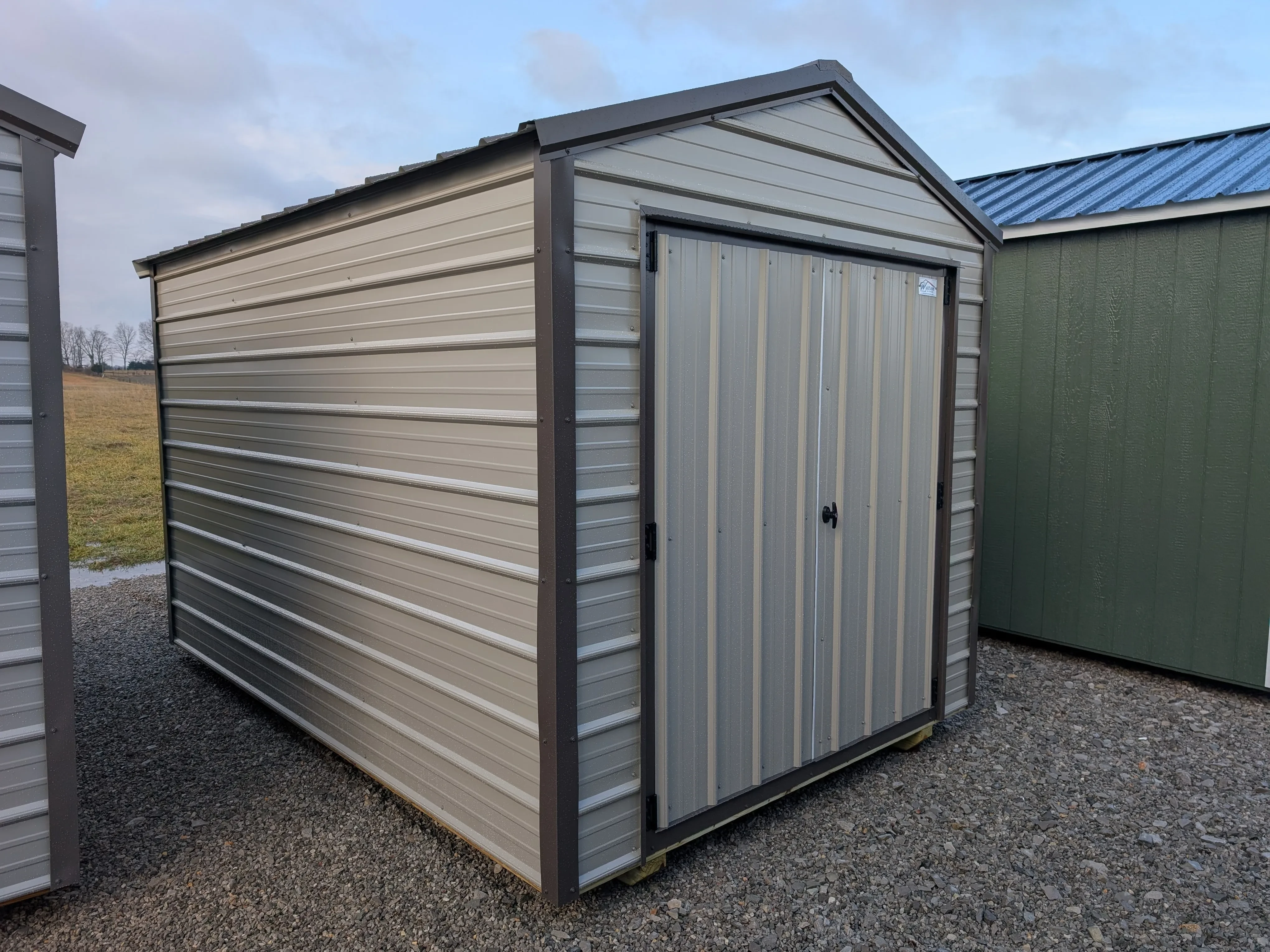 a clay colored metal utility shed with double doors sitting in the gravel