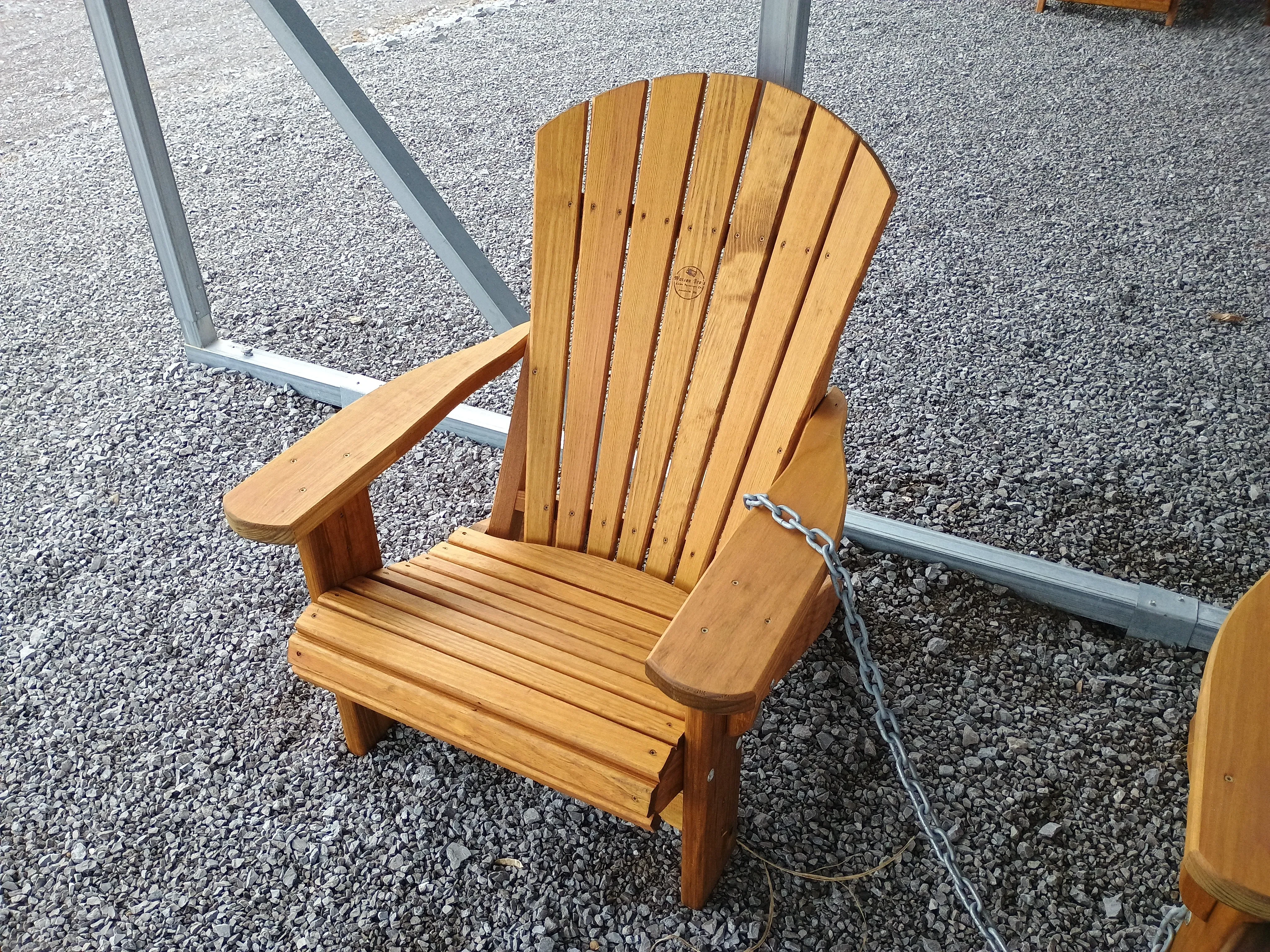 a wood stained and sealed chair sitting in the gravel. It is chained up to other furniture
