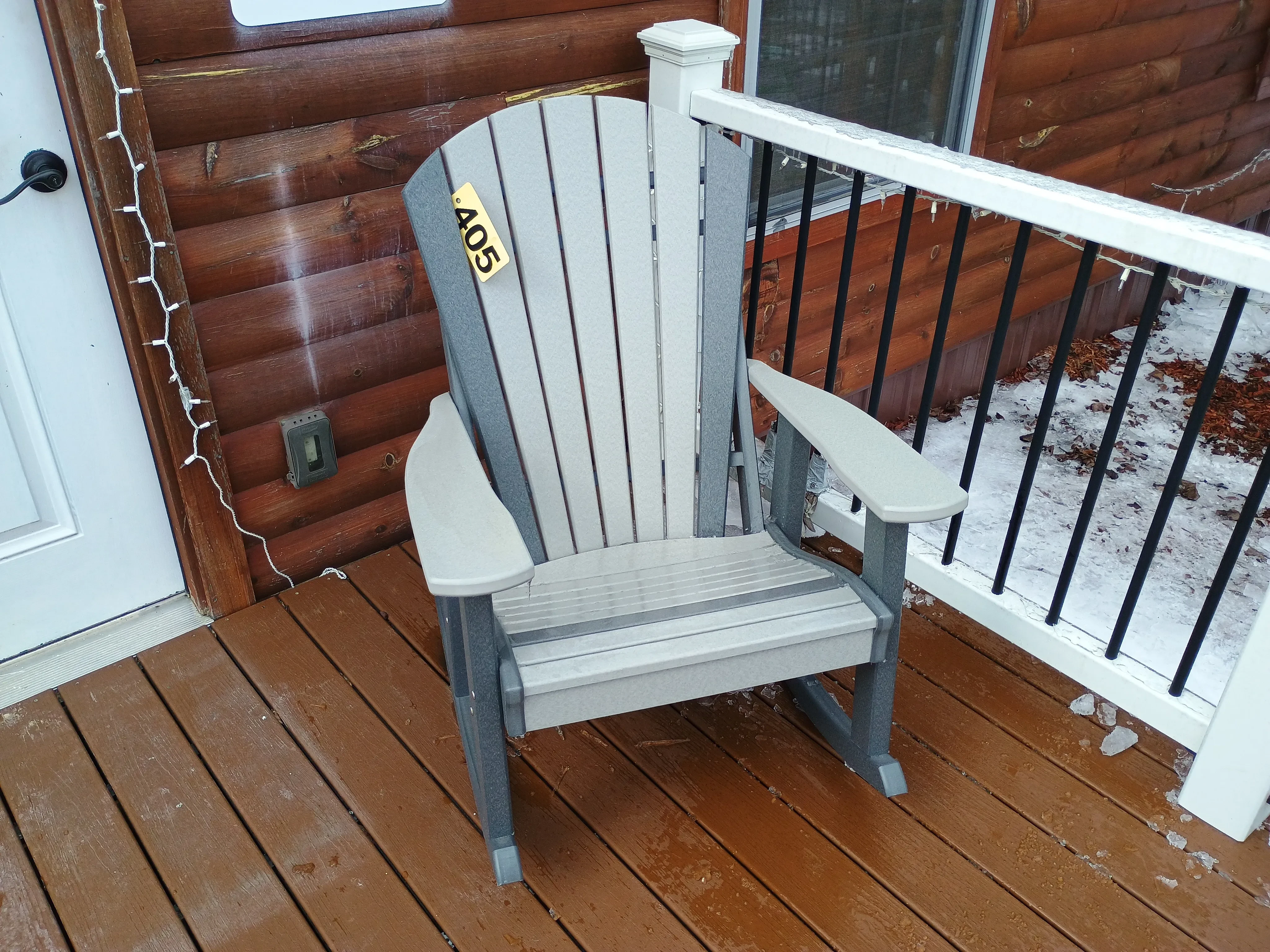 a light gray rocking chair sitting on a porch. It has dark gray accents and there is snow on the ground nearby
