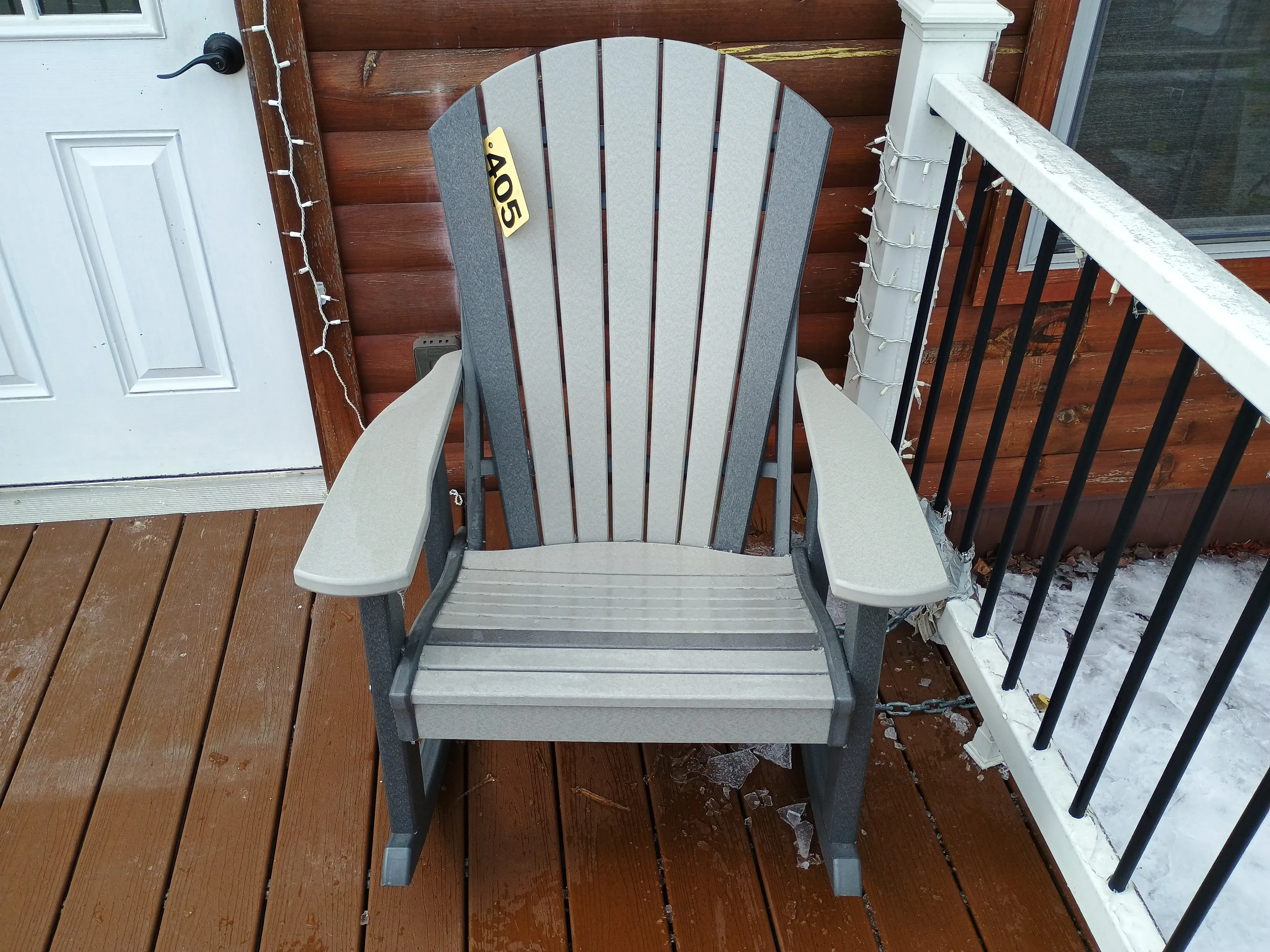 a rocking chair sitting on a wood porch. It is light gray with dark gray accents