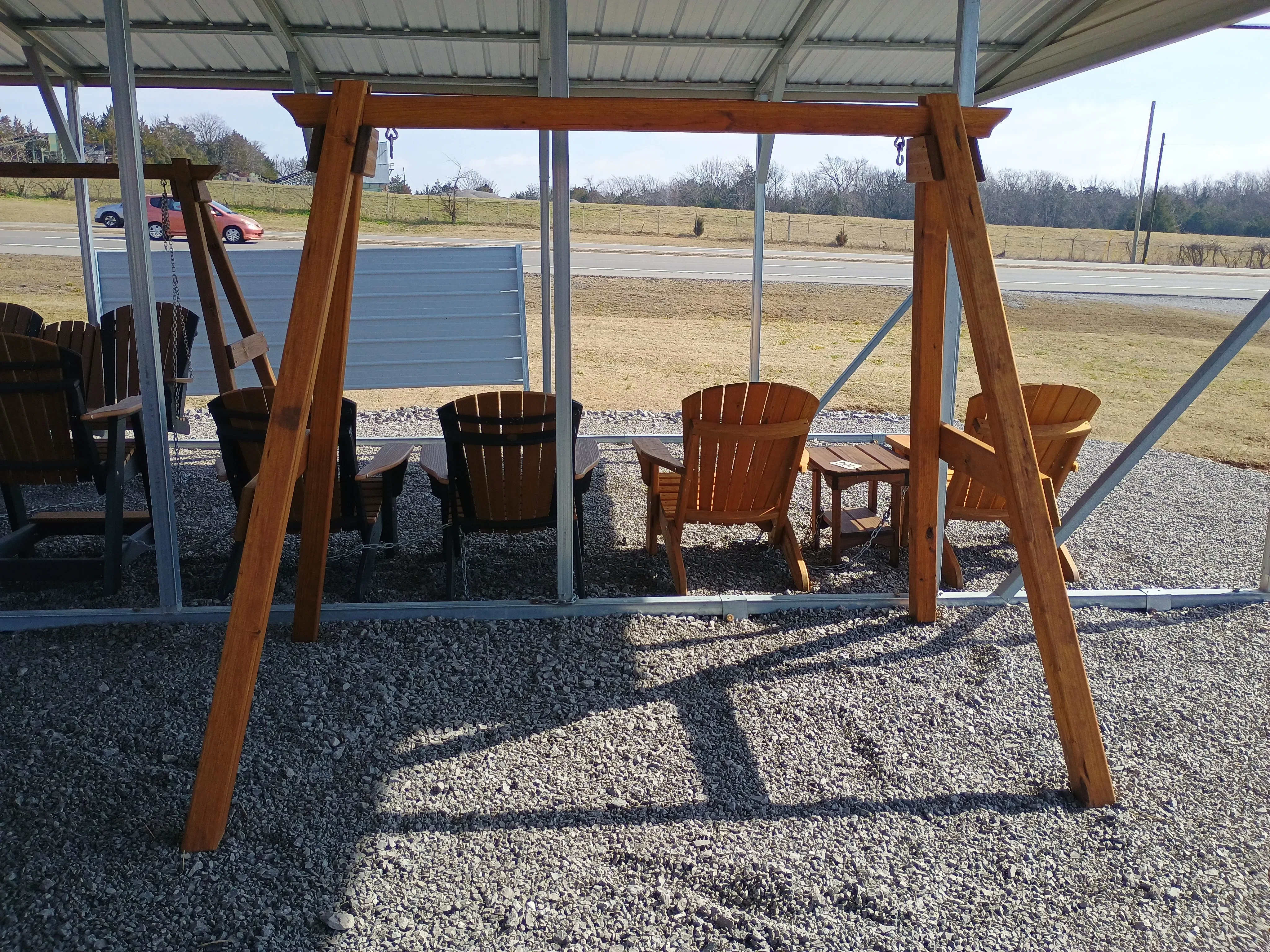 a wooden a-frame structure standing in the gravel. There are wood chairs behind it
